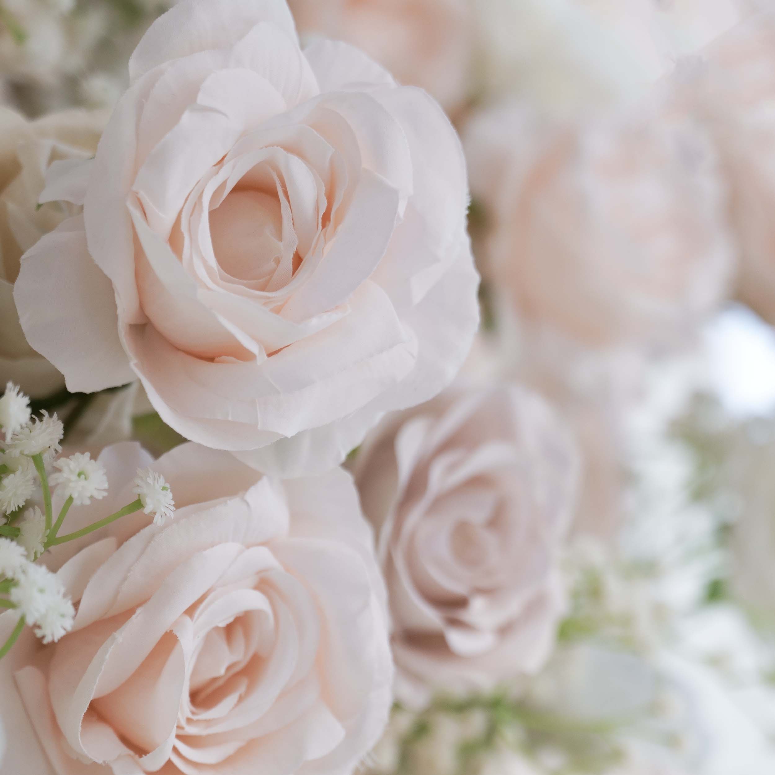 This close - up image highlights a section of a floral backdrop. The flowers predominantly include artificial roses in soft, pastel shades such as light pink and off - white. Delicate sprigs of baby&