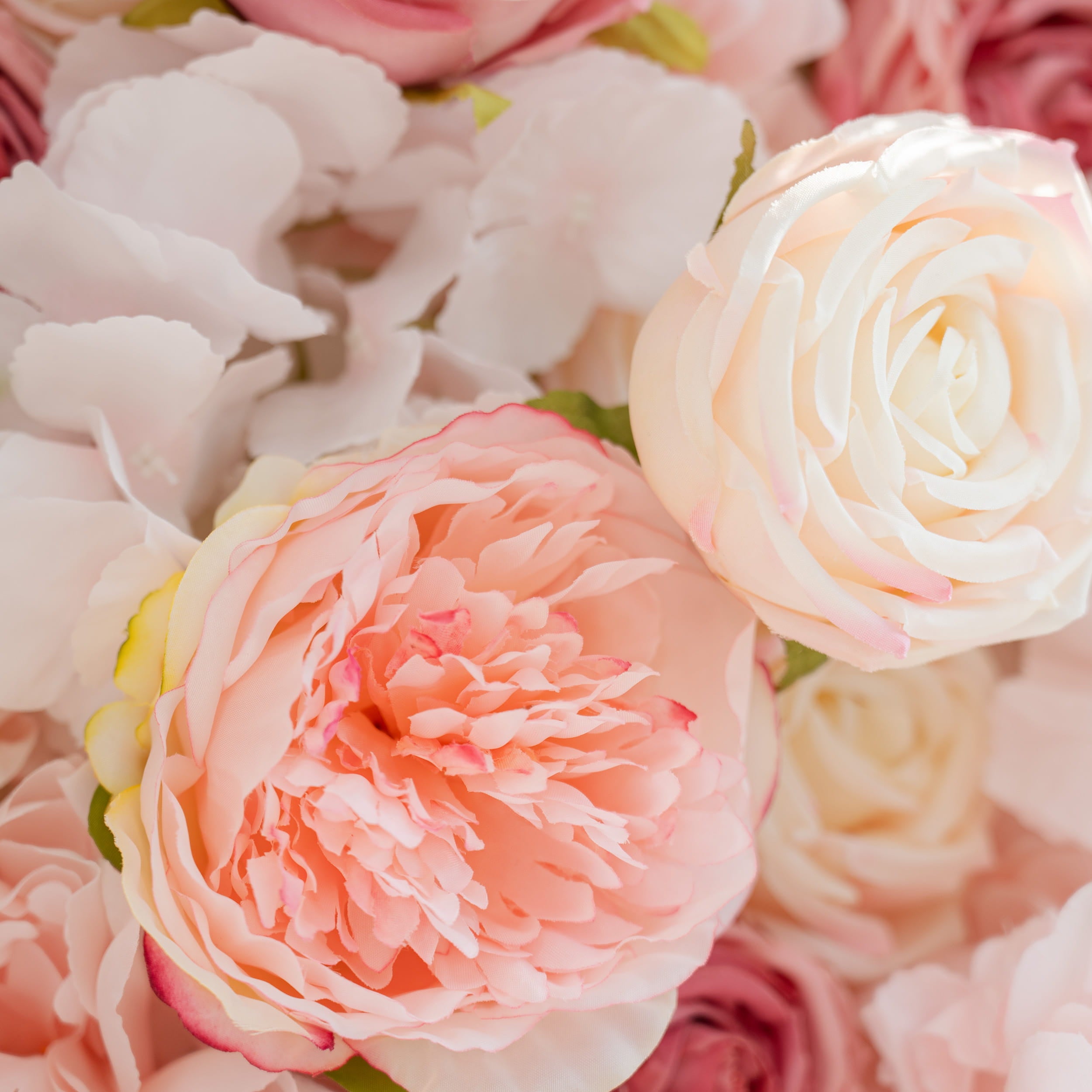 A close - up of two types of flowers: a pink peony with soft petals and a creamy - white rose. They are part of a larger arrangement of pastel - colored blooms.