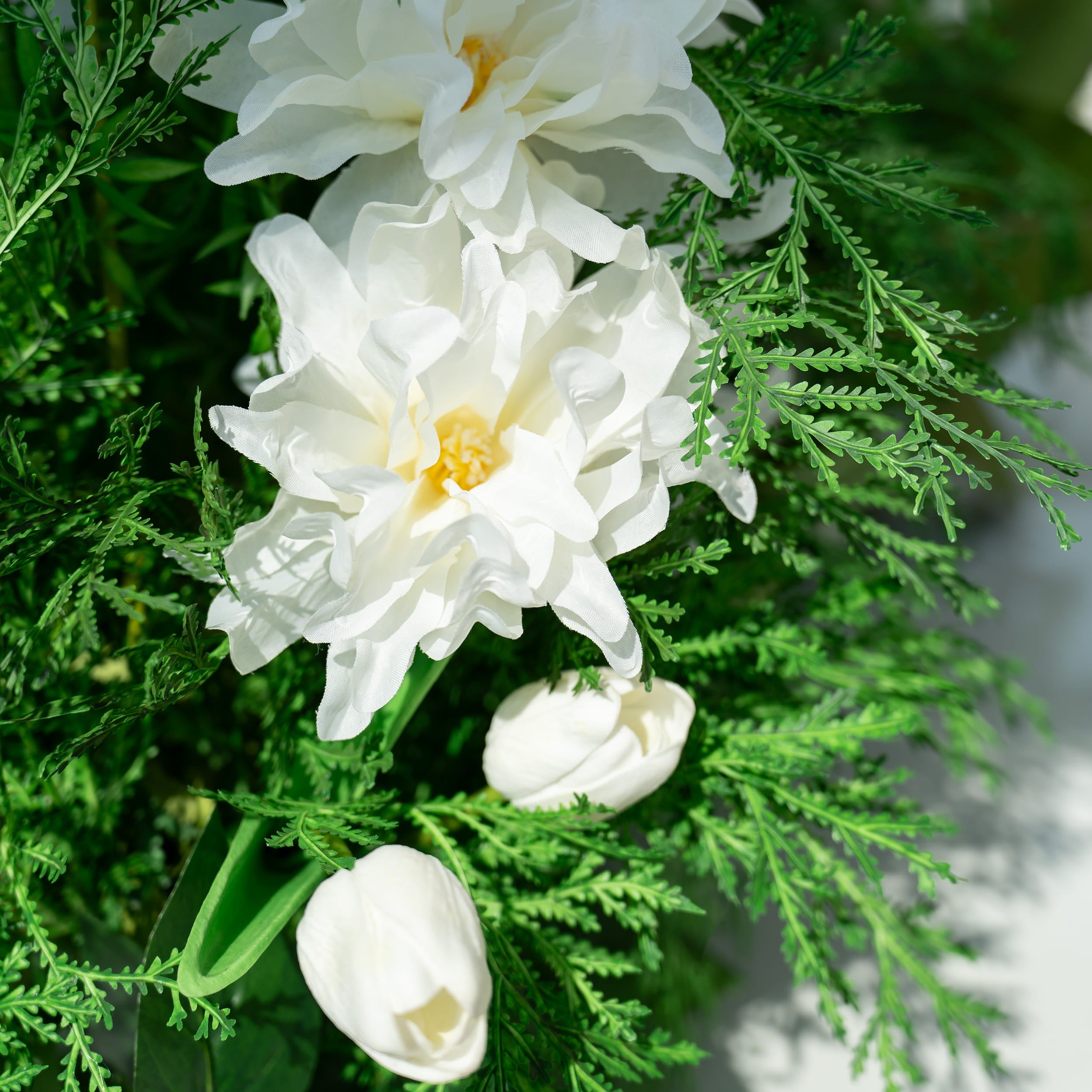 The floral arrangement features a variety of white flowers, including peonies and tulips, surrounded by lush green foliage. This elegant composition is ideal for weddings, creating a romantic and sophisticated atmosphere.