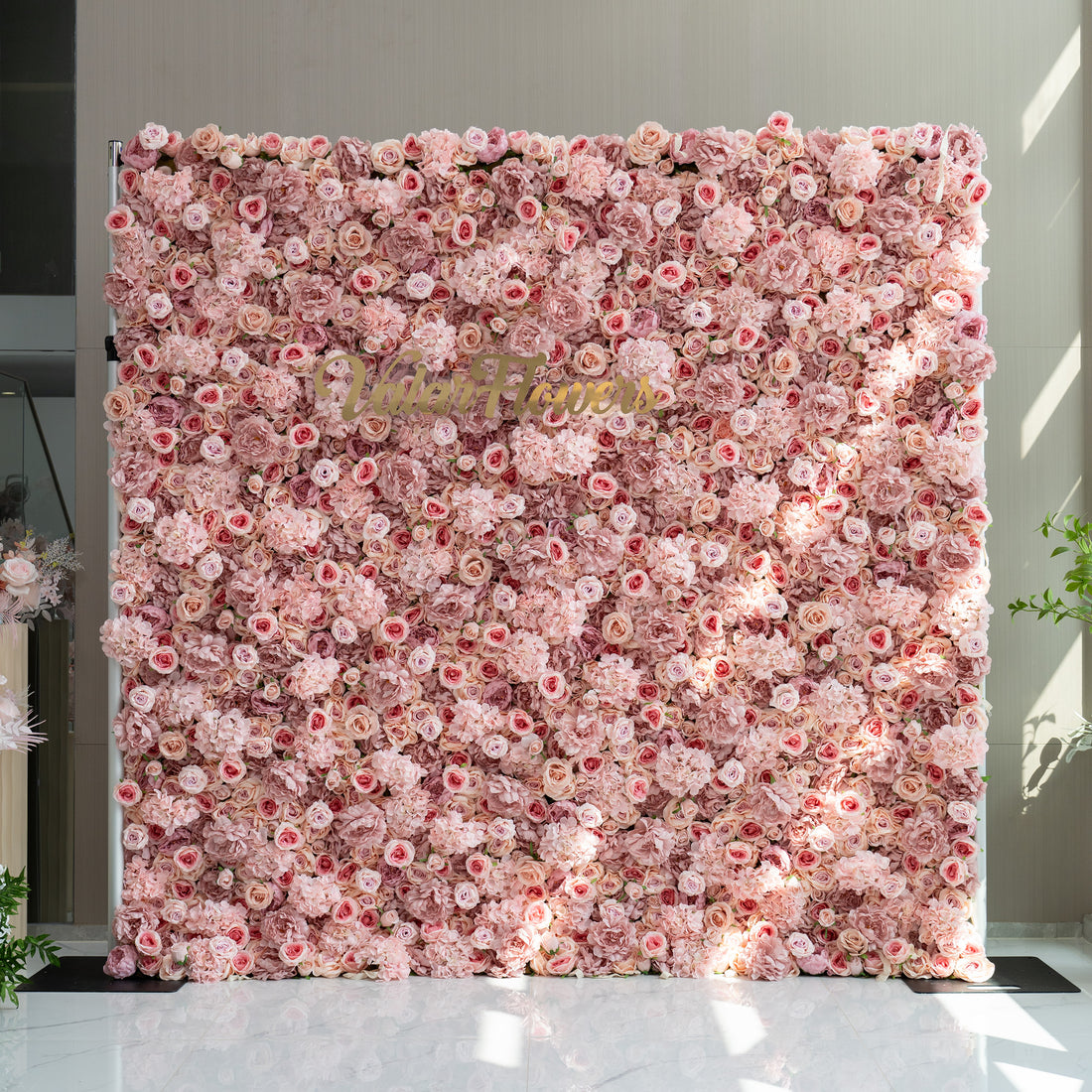 This image features a stunning floral wall adorned with a plethora of light pink and rose - colored flowers. In the center of the wall, the brand name "ValarFlowers" is displayed in elegant gold lettering. The overall ambiance is soft, romantic, and inviting, making it ideal for events such as weddings, bridal showers, or romantic celebrations.