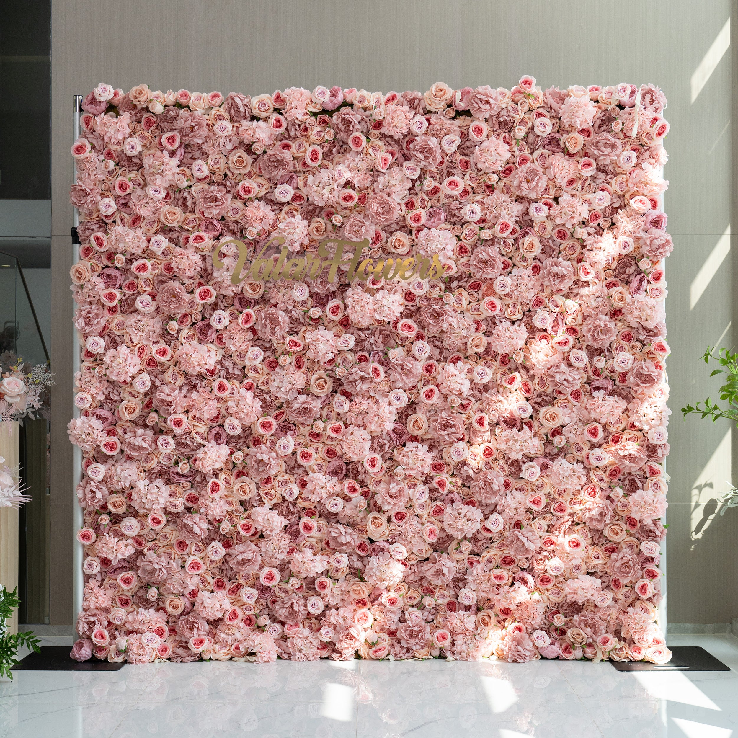 This image features a stunning floral wall adorned with a plethora of light pink and rose - colored flowers. In the center of the wall, the brand name "ValarFlowers" is displayed in elegant gold lettering. The overall ambiance is soft, romantic, and inviting, making it ideal for events such as weddings, bridal showers, or romantic celebrations.