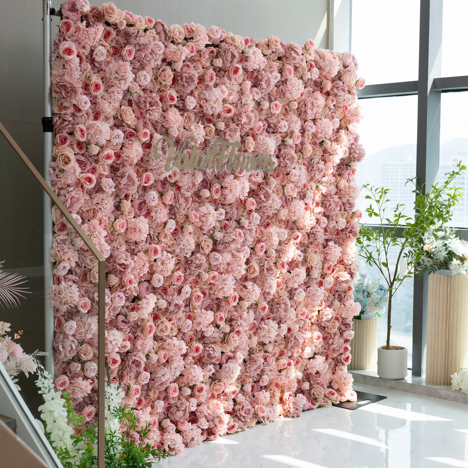 This image features a stunning floral wall adorned with a dense arrangement of light pink and peach - colored flowers. The wall is part of a display that includes the brand name "ValarFlowers" prominently displayed in the center. The overall ambiance is soft, romantic, and inviting, making it ideal for events such as weddings, bridal showers, or romantic celebrations.