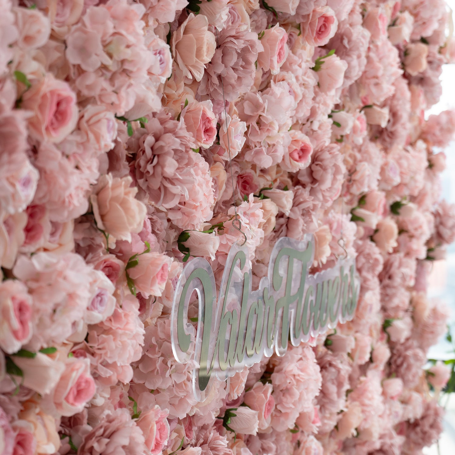 The image features a lush, pink floral wall with the text "ValarFlowers" prominently displayed in the center. The flowers are densely packed, creating a soft and romantic backdrop.