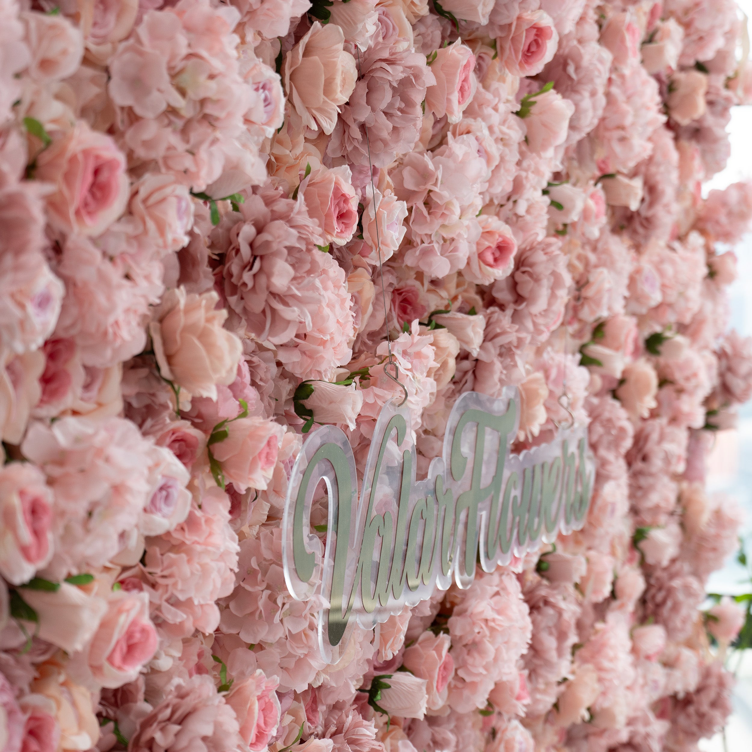 The image features a lush, pink floral wall with the text "ValarFlowers" prominently displayed in the center. The flowers are densely packed, creating a soft and romantic backdrop.