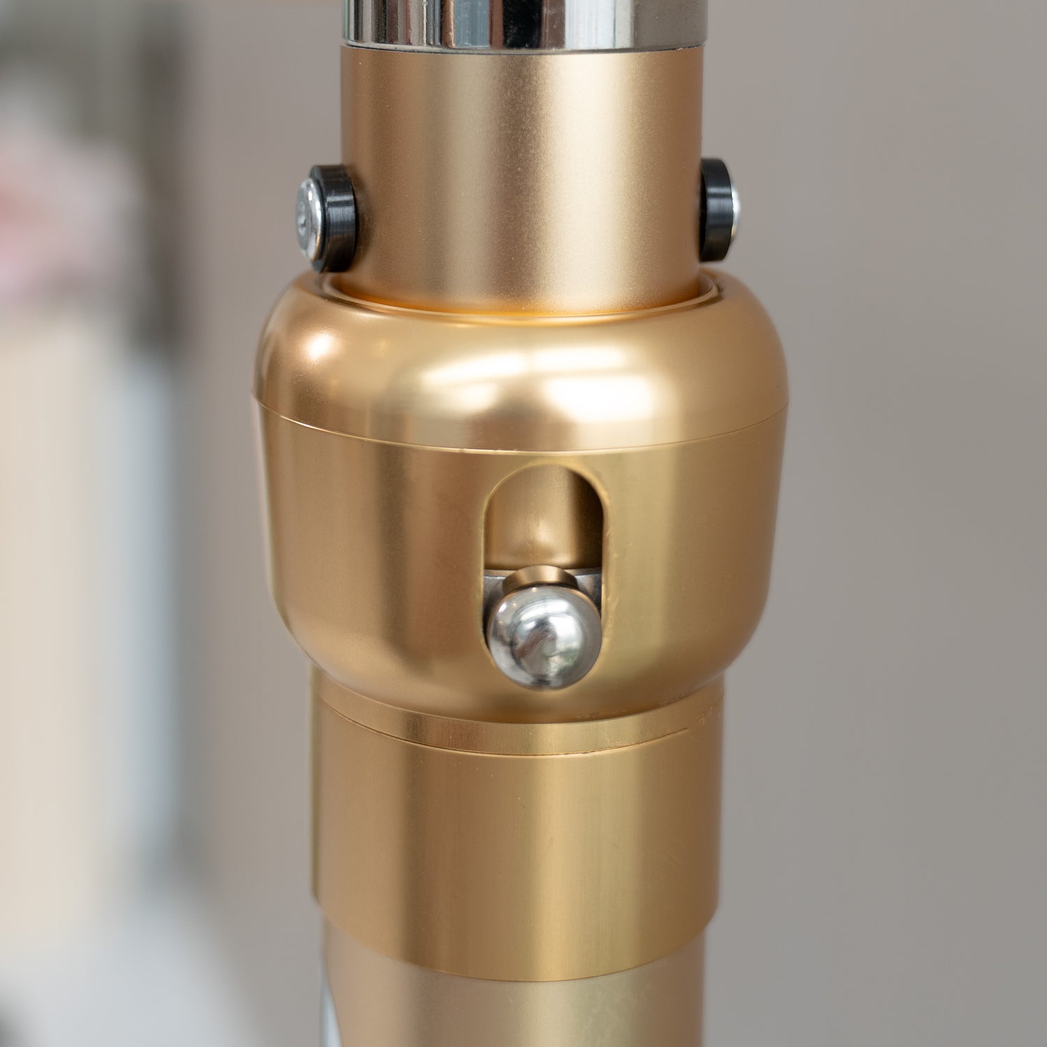 This image showcases a close - up of a metallic rod structure component. The piece is predominantly gold - colored with a smooth, polished finish. It features two black - capped screws near the top, likely for securing or adjusting purposes. There is also a prominent silver - colored spherical knob in the center, set within an oval - shaped cut - out. The design suggests it could be part of a stand or framework, perhaps for decorative or photographic equipment.