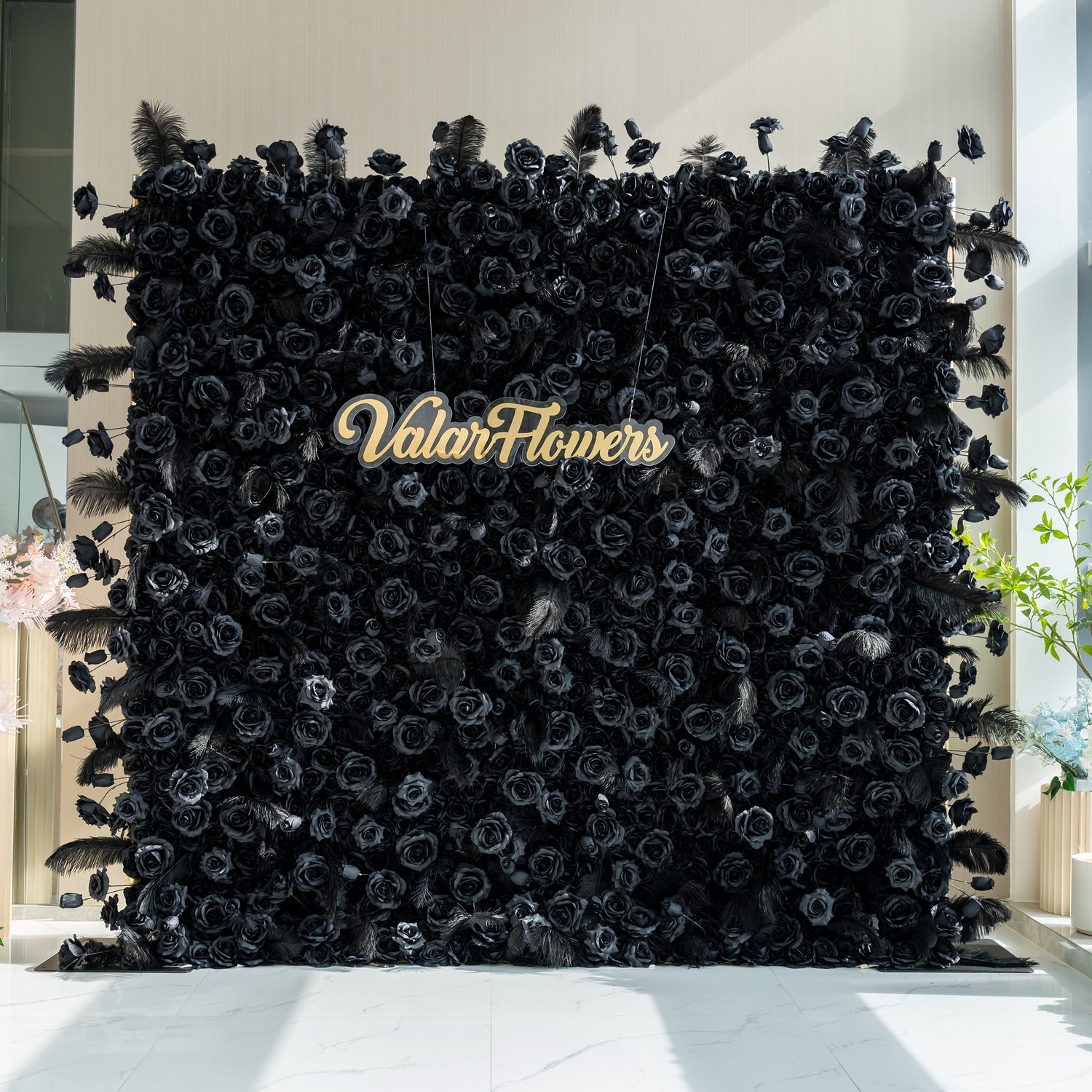 The image features a striking black floral wall with the name "ValarFlowers" prominently displayed in the center. The wall is adorned with black roses and feathers, creating a dramatic and elegant look.
