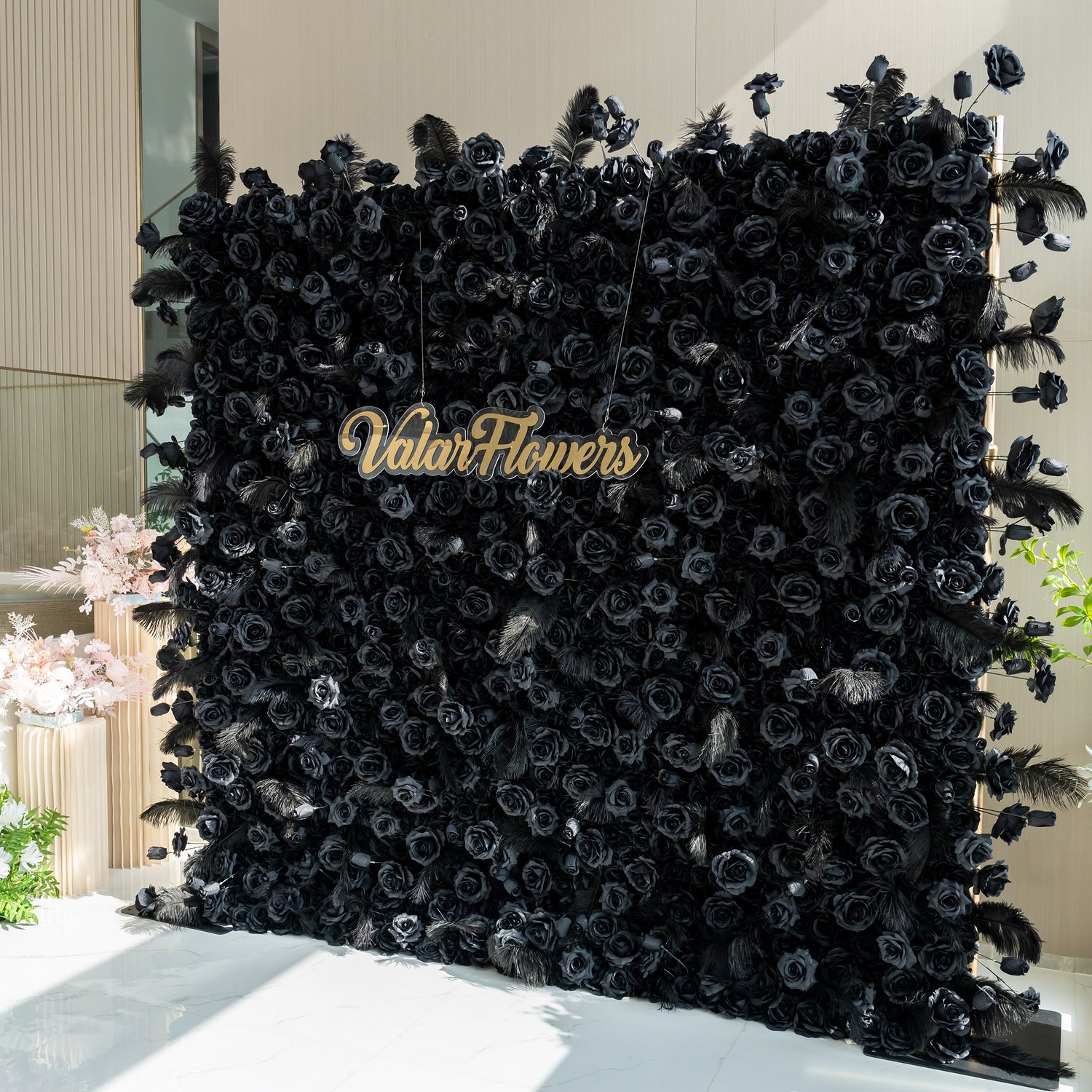 The image showcases a stunning black rose wall with the brand name "ValarFlowers" prominently displayed in the center. The wall is adorned with feathers at the edges, adding an elegant touch.