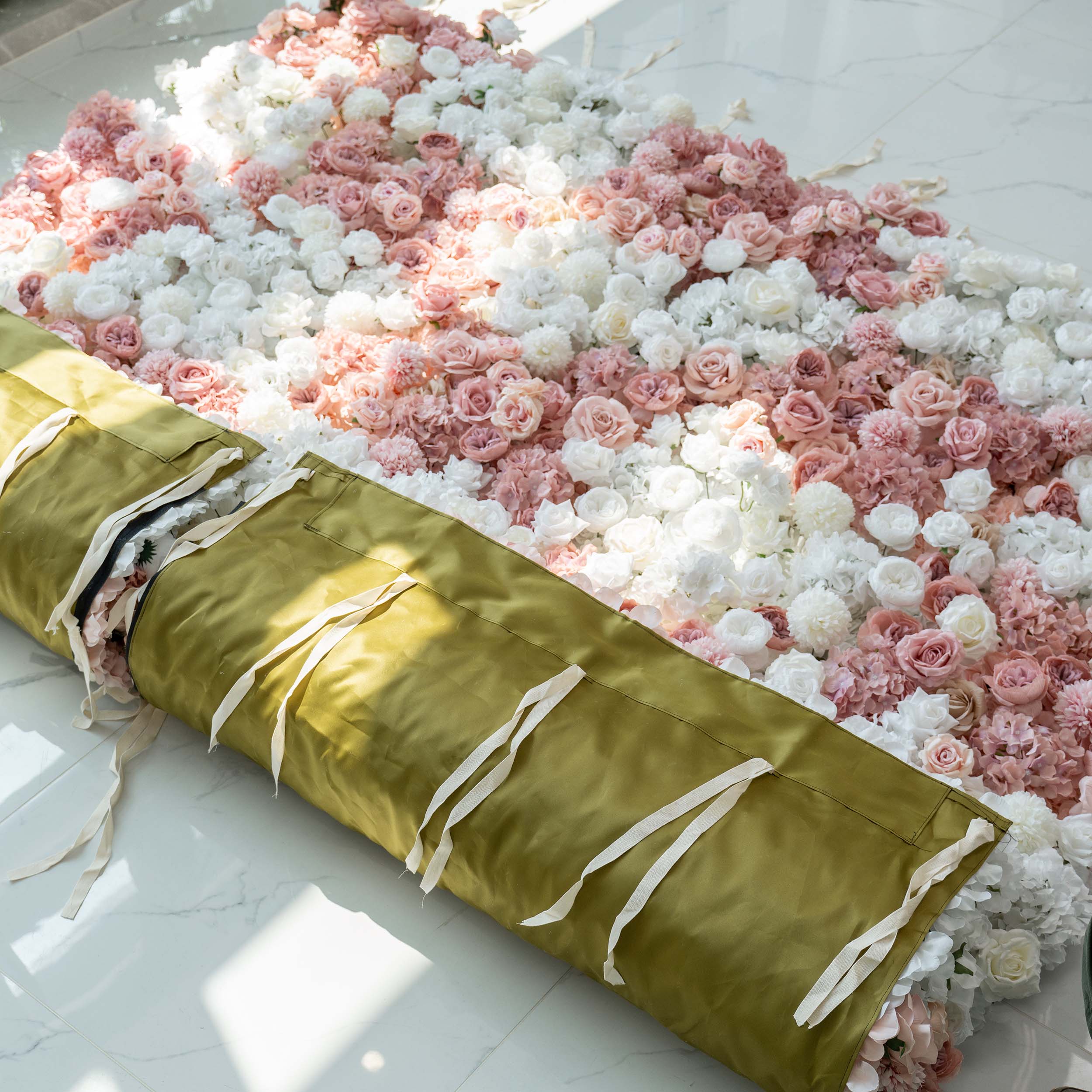 A rolled - up floral panel with a mix of white and pink roses and hydrangeas. The back features a green fabric with white ties, ready for setup.