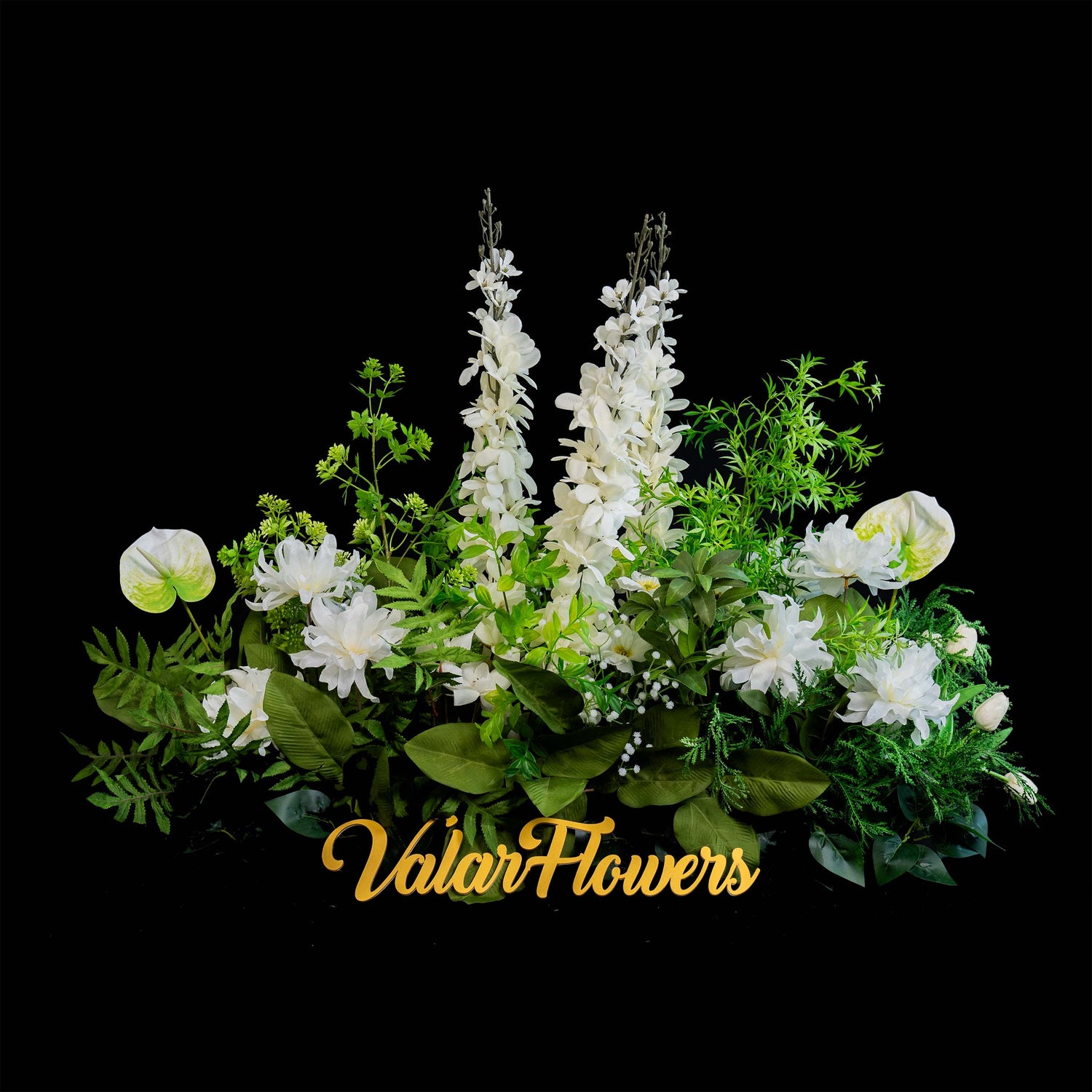 A lush floral arrangement by ValarFlowers showcases tall white spires surrounded by various white blooms and green foliage, all set against a stark black background for a dramatic effect.