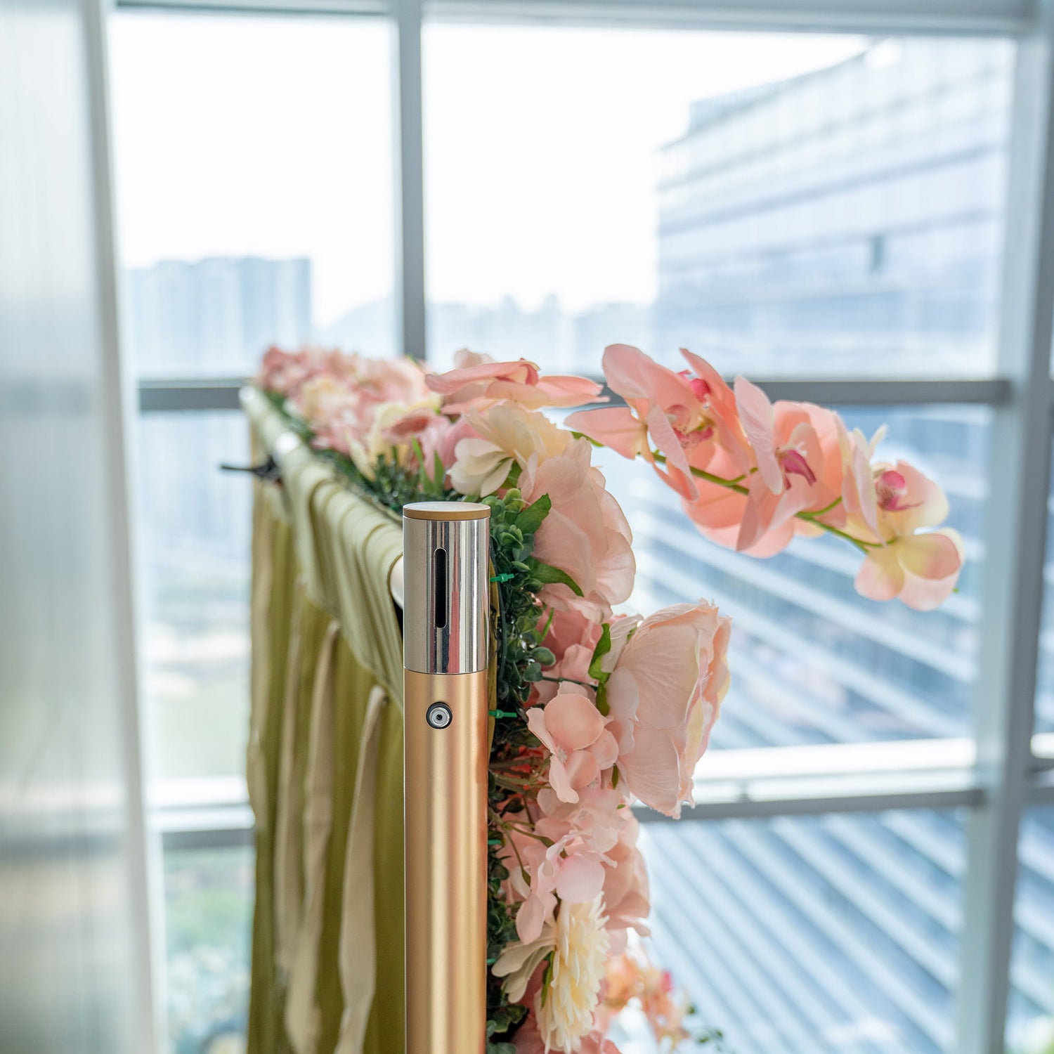 The image features a decorative setup with artificial pink orchids and other pastel - hued flowers arranged along a pole and green fabric. There&