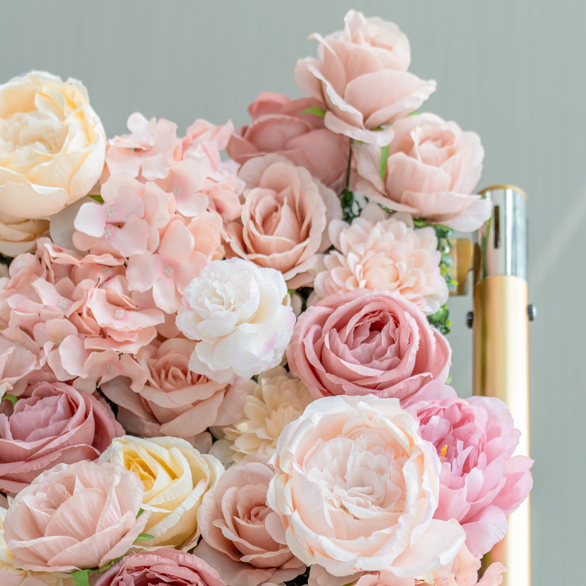 This close - up features artificial roses, peonies, and hydrangeas in soft pastel colors like pink, peach, and cream. The arrangement, beside a gold - toned pole, has a romantic and elegant style.