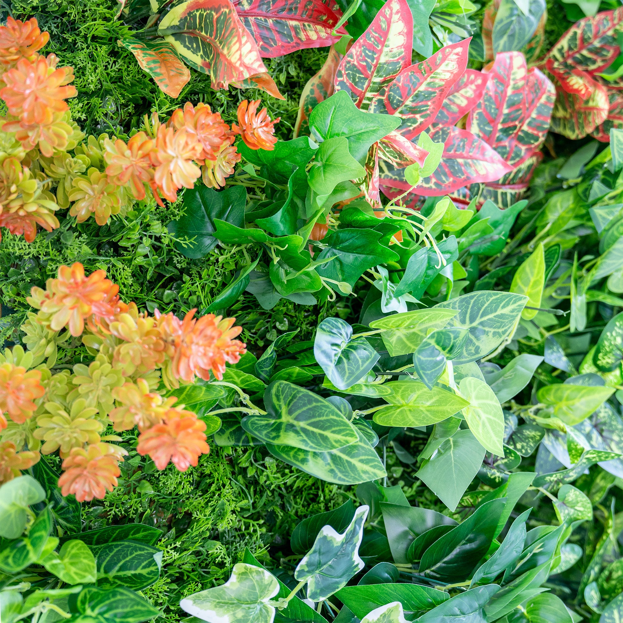 This image showcases a lush arrangement of artificial greenery. It prominently features various types of ferns in different shades of green, from light lime to deeper emerald hues. Interspersed among the ferns are broad - leafed plants, adding texture and variety to the display. The overall effect is a vibrant, natural - looking cluster of foliage, ideal for decorative purposes, such as event backdrops or interior decor.