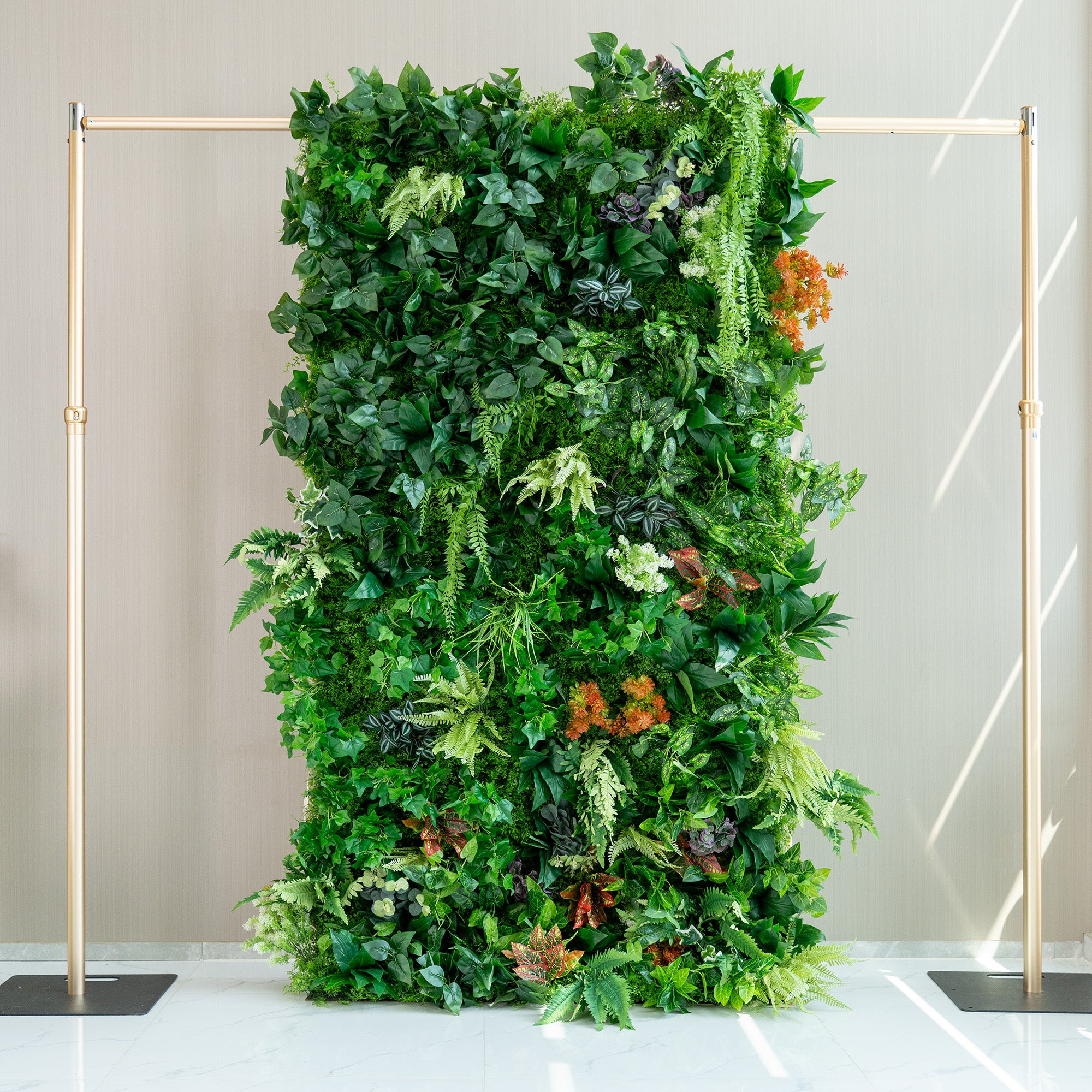 This image features a lush, artificial green wall supported by a metallic gold frame. The wall is densely packed with a variety of faux plants, showcasing different shades of green foliage. There are also splashes of color from orange, red, and purple - hued plants, adding visual interest. The overall effect is a vibrant, natural - looking backdrop, ideal for decorative purposes in indoor spaces.