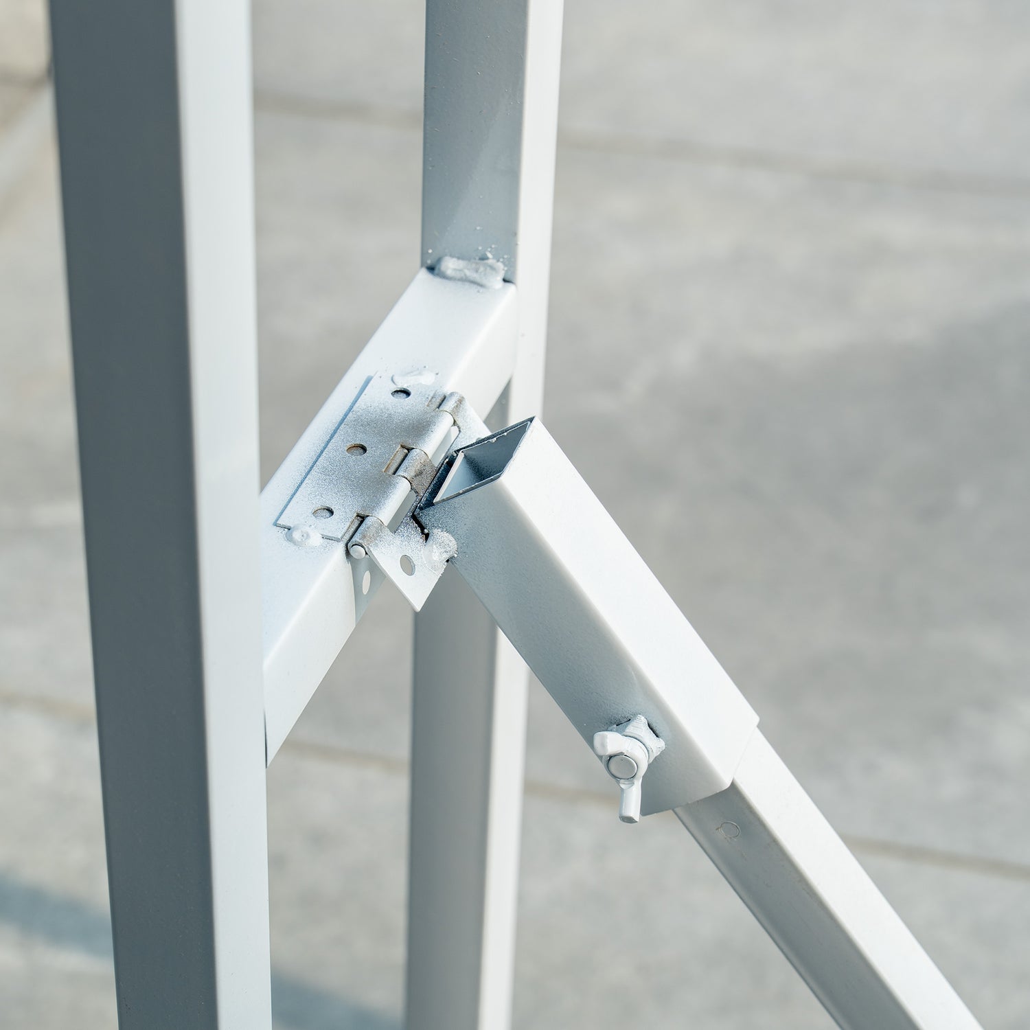 This backdrop stand is a metallic structure with a light - colored finish. It features a hinge mechanism, as seen in the image, which likely allows for folding or adjustment. The stand has a simple, sturdy design with a rectangular frame and diagonal support, secured with bolts and metal plates for stability.