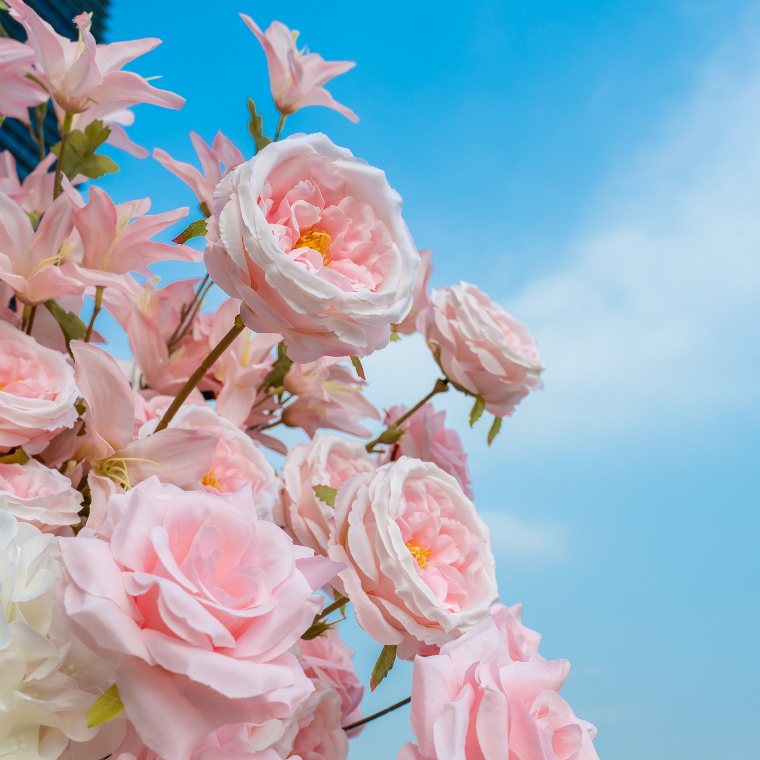 This backdrop features a cluster of artificial flowers set against a clear blue sky. The main flowers are delicate pink roses with soft, ruffled petals. Accompanied by some light - pink star - shaped flowers, the color palette is dominated by gentle shades of pink. The style is romantic and dreamy, perfect for wedding or garden - themed events.