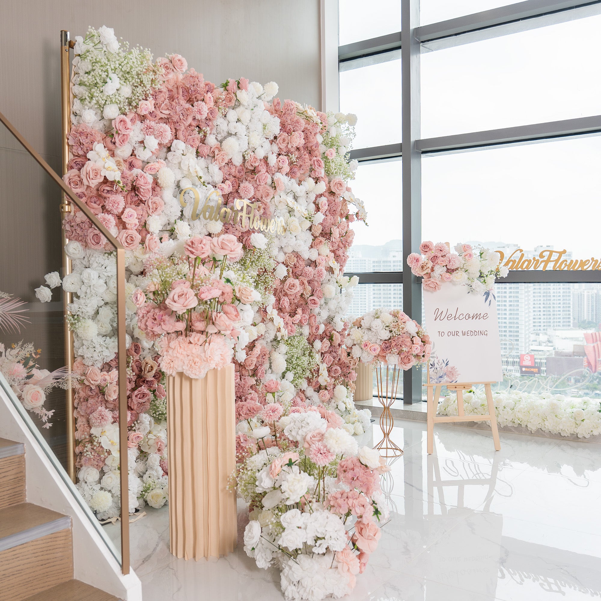 This backdrop is a lush floral wall, perfect for a wedding setting as indicated by the “Welcome to our wedding” sign. It features a mix of artificial roses in soft pinks and whites, along with white hydrangeas and baby&