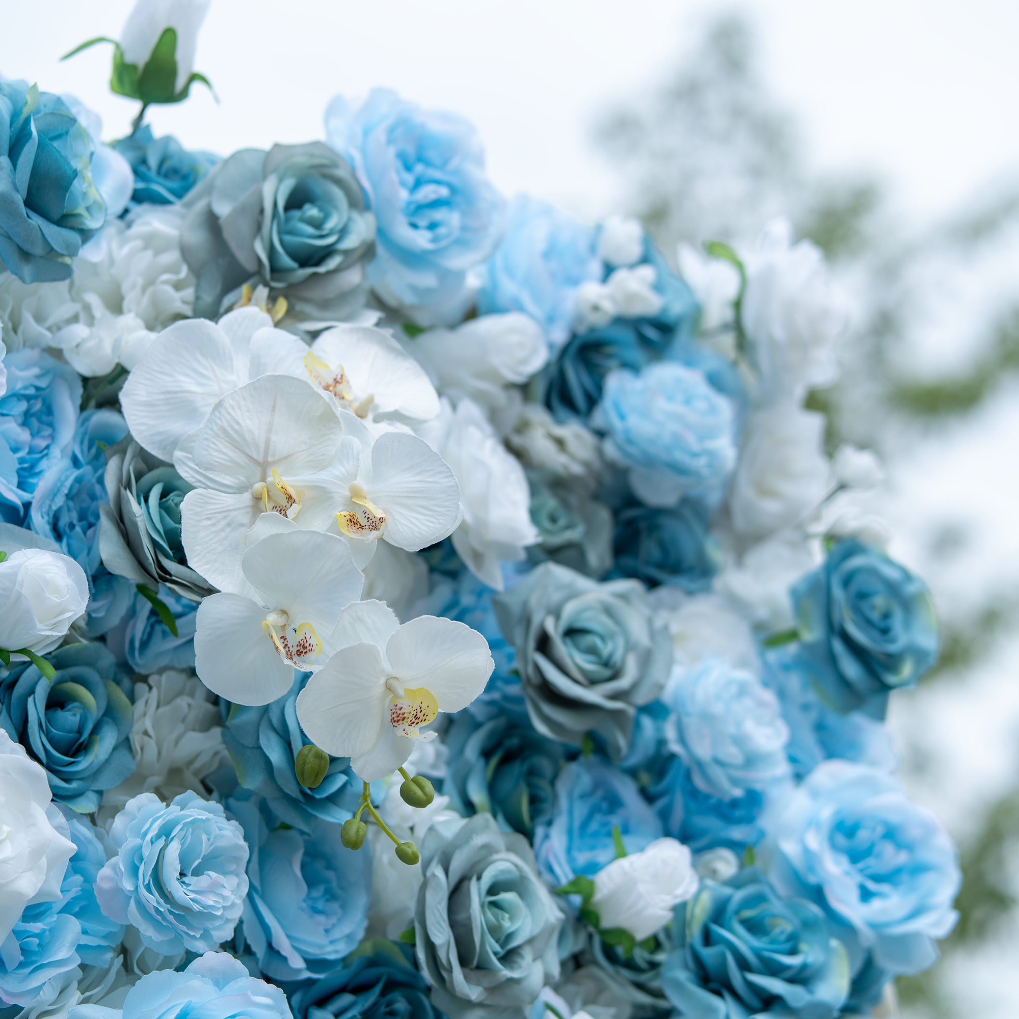 This photo captures a lush, vibrant floral arrangement. It features a mix of blue and white roses, with the blue hues ranging from light to deep tones. Interspersed among the roses are white orchids, their large, delicate petals and yellow - speckled centers standing out prominently. The dense clustering of flowers creates a rich, textured appearance, exuding an air of elegance and sophistication, perfect for high - end events.