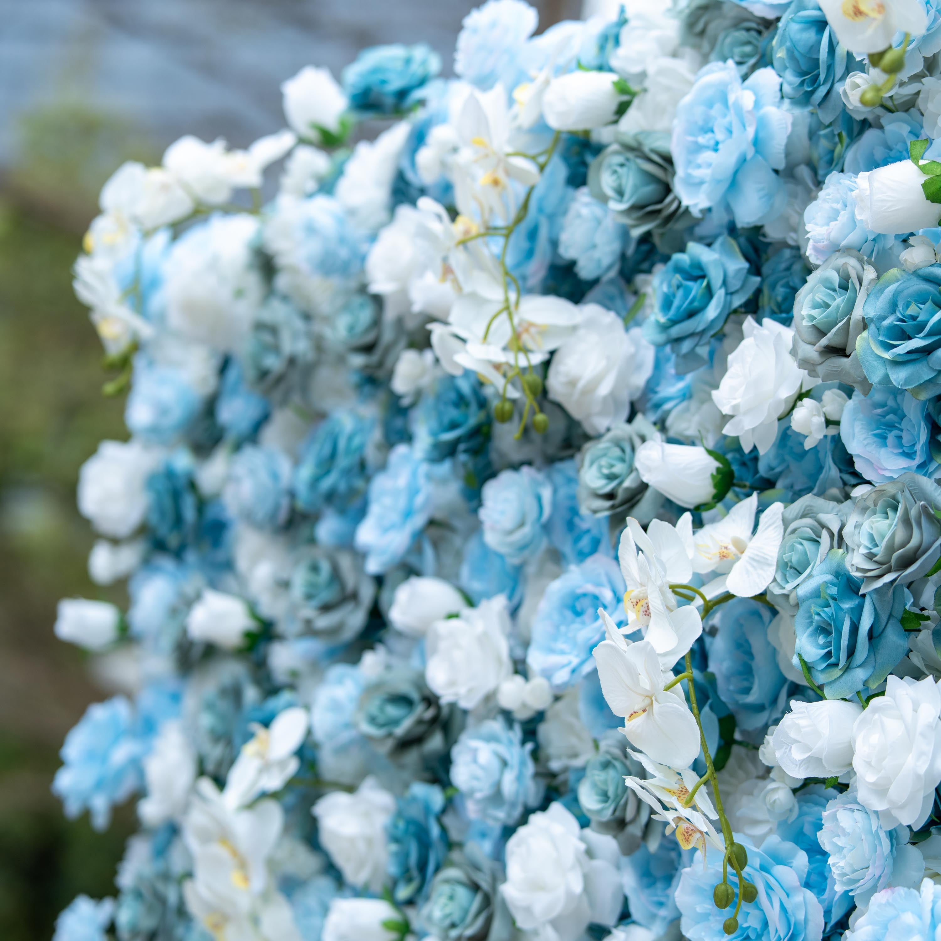 This photo showcases a lush floral arrangement featuring a beautiful blend of blue and white roses, complemented by elegant white orchids. The varying shades of blue and white create a visually soothing and harmonious effect. The roses&