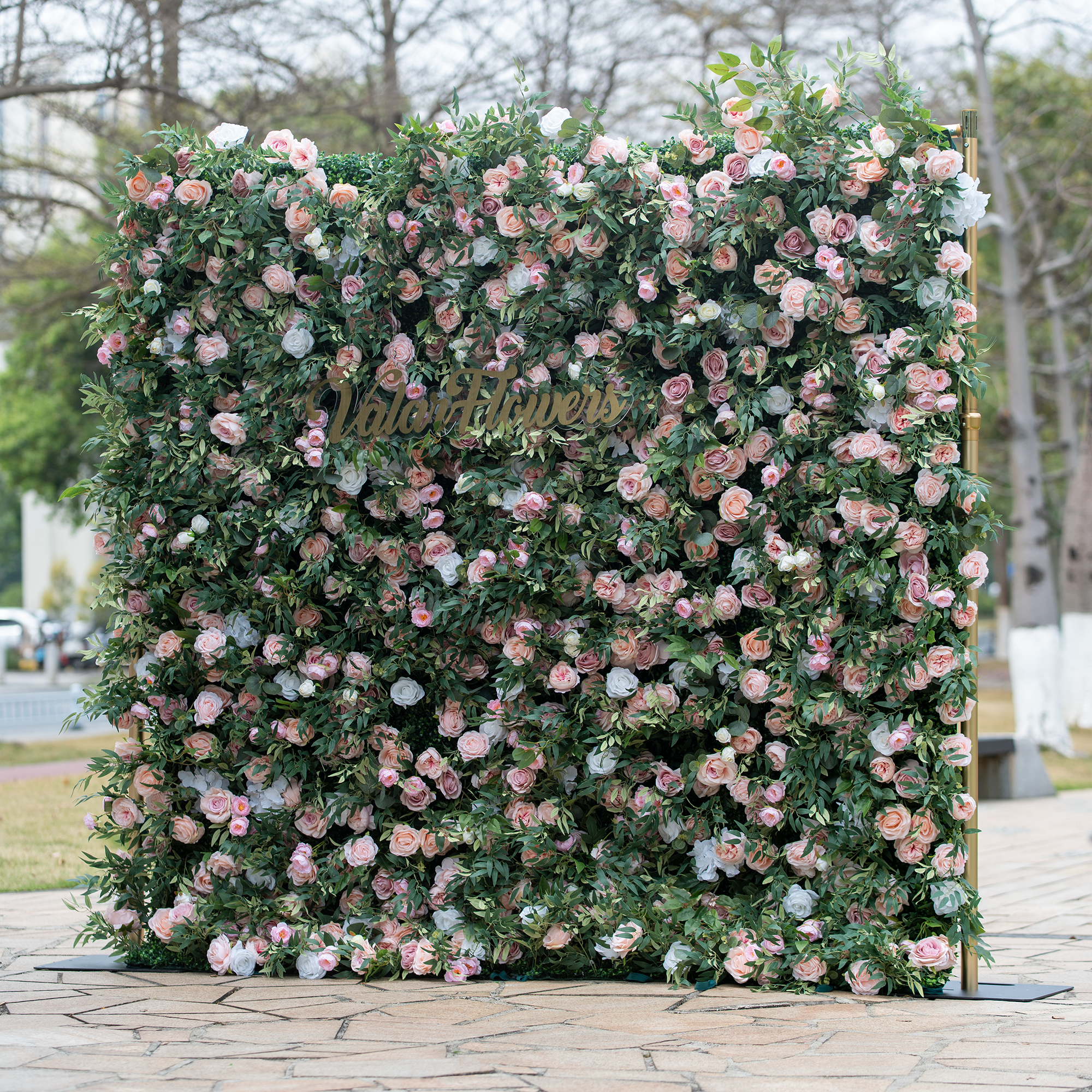 This photo showcases a large floral backdrop brimming with pink and white roses, interspersed with lush green foliage. In the center, golden lettering reads "ValarFlowers". Ideal for events like bridal showers or garden - themed corporate functions, it fits a "Romantic Garden Soirée" theme. The soft hues and dense arrangement exude elegance and charm, making it a perfect decorative piece.