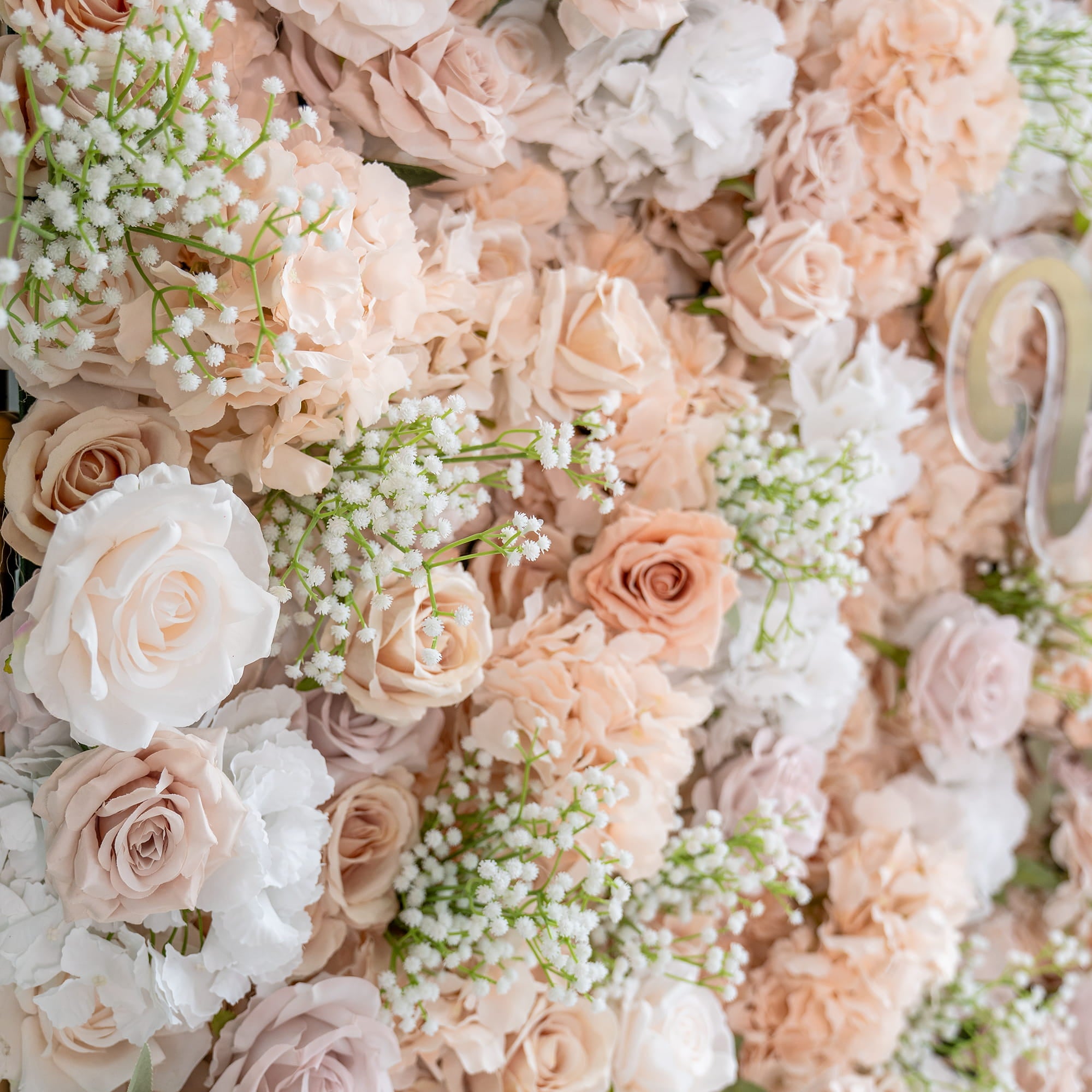 This floral backdrop features a lush arrangement of artificial flowers. Predominant blooms include roses in soft hues of blush, cream, and pale pink, interspersed with delicate sprigs of baby&