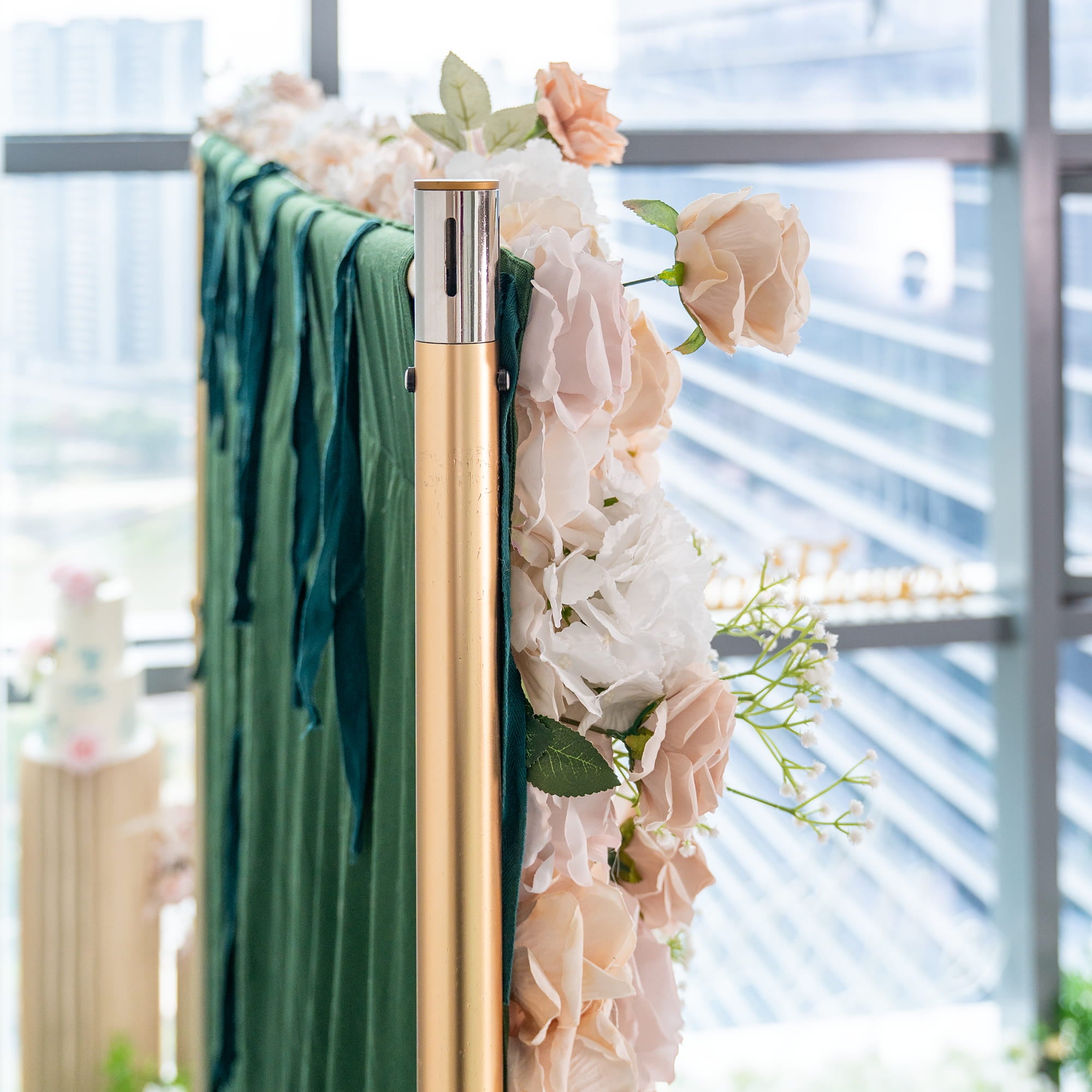 This backdrop combines a lush green fabric with an arrangement of artificial flowers. The flowers include roses in soft shades of white and blush, along with delicate sprigs of baby&