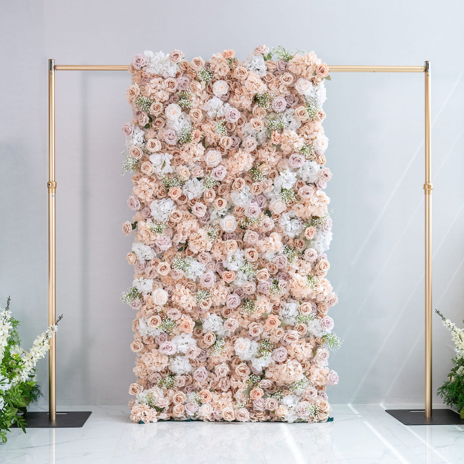 This floral backdrop is supported by a gold - toned metal frame. It is densely covered with artificial flowers, mainly roses in soft shades of blush, cream, and pale pink, along with white hydrangeas and delicate sprigs of baby&