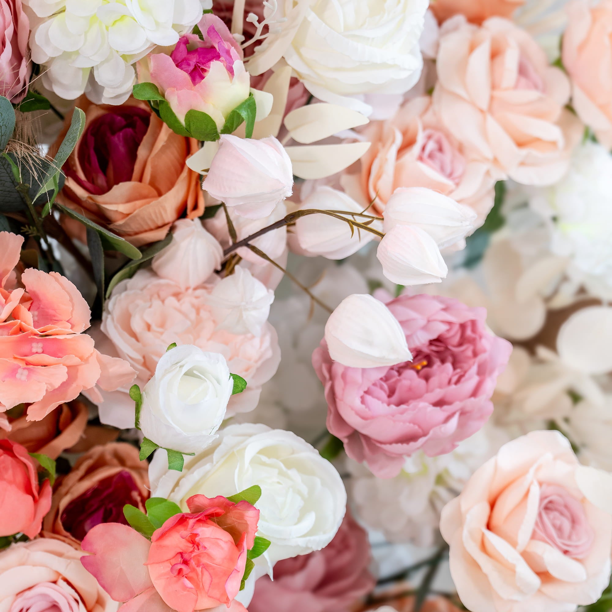This backdrop features a lush arrangement of artificial flowers in a soft, pastel color palette. It includes roses in shades of white, pink, and peach, along with peonies and other assorted blooms. Eucalyptus leaves add a touch of green, enhancing the romantic and elegant style, perfect for wedding or event decor.