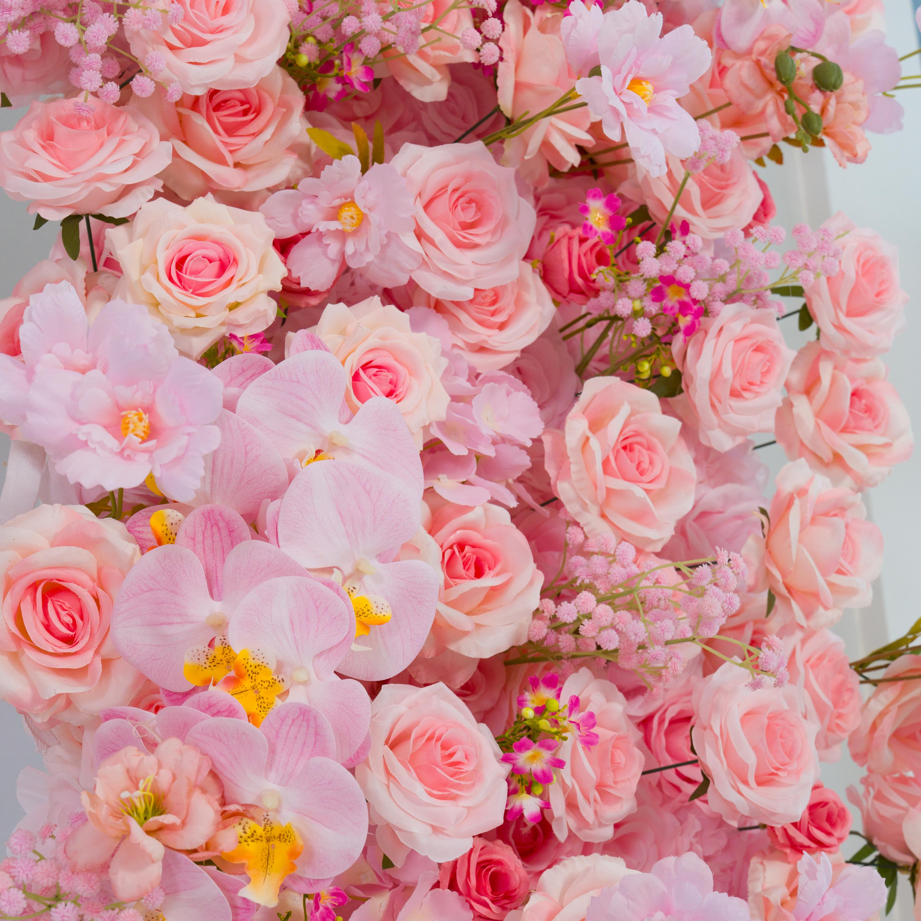 This backdrop is a lush, colorful display of artificial flowers. It features a variety of pink - hued blooms, including delicate pink roses, large - petaled pink orchids with yellow - spotted centers, and small clusters of pink baby&
