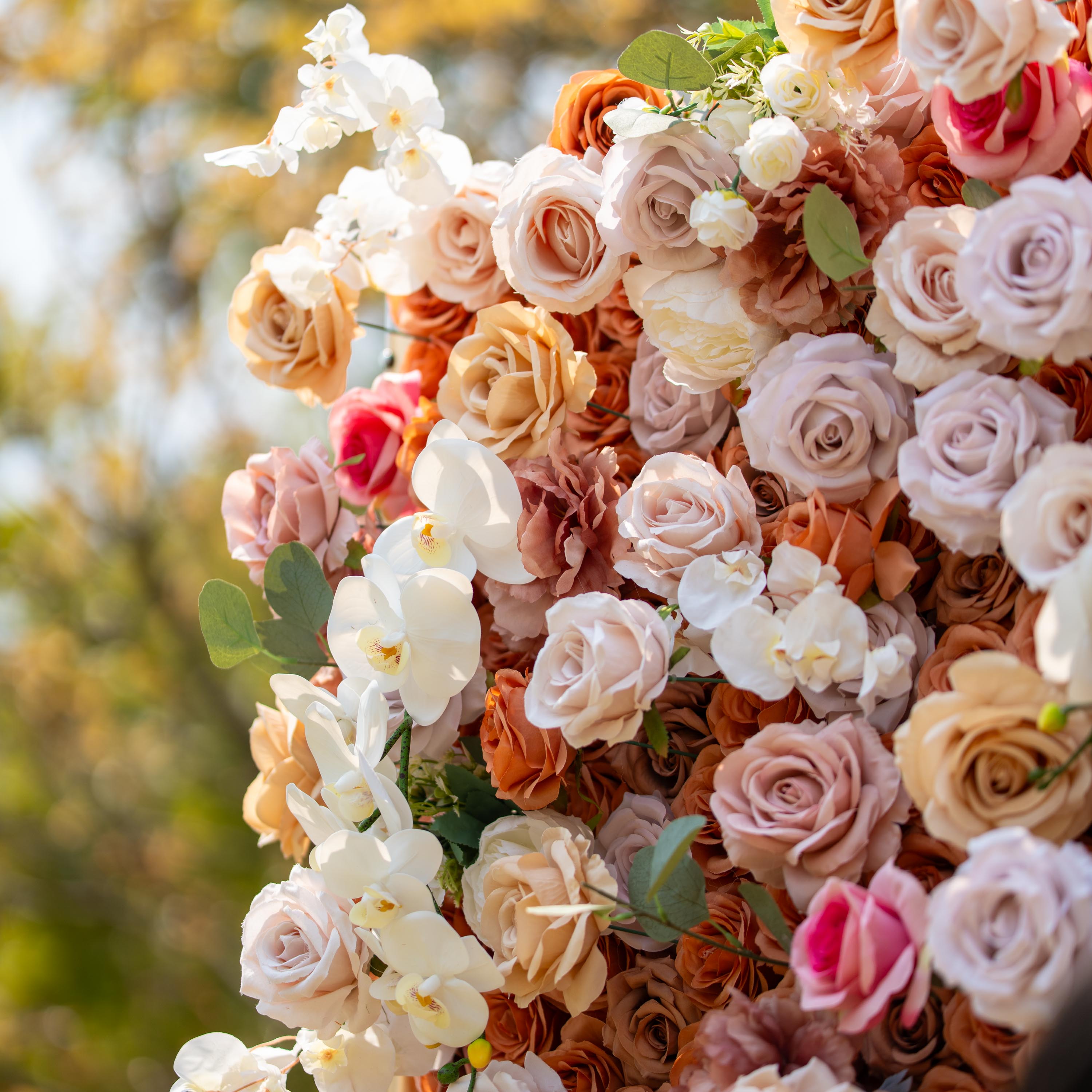 This backdrop features a warm, earthy theme with colors like beige, cream, and soft brown. It is densely adorned with roses and white orchids. Ideal for elegant events such as weddings, upscale garden parties, or refined corporate celebrations.