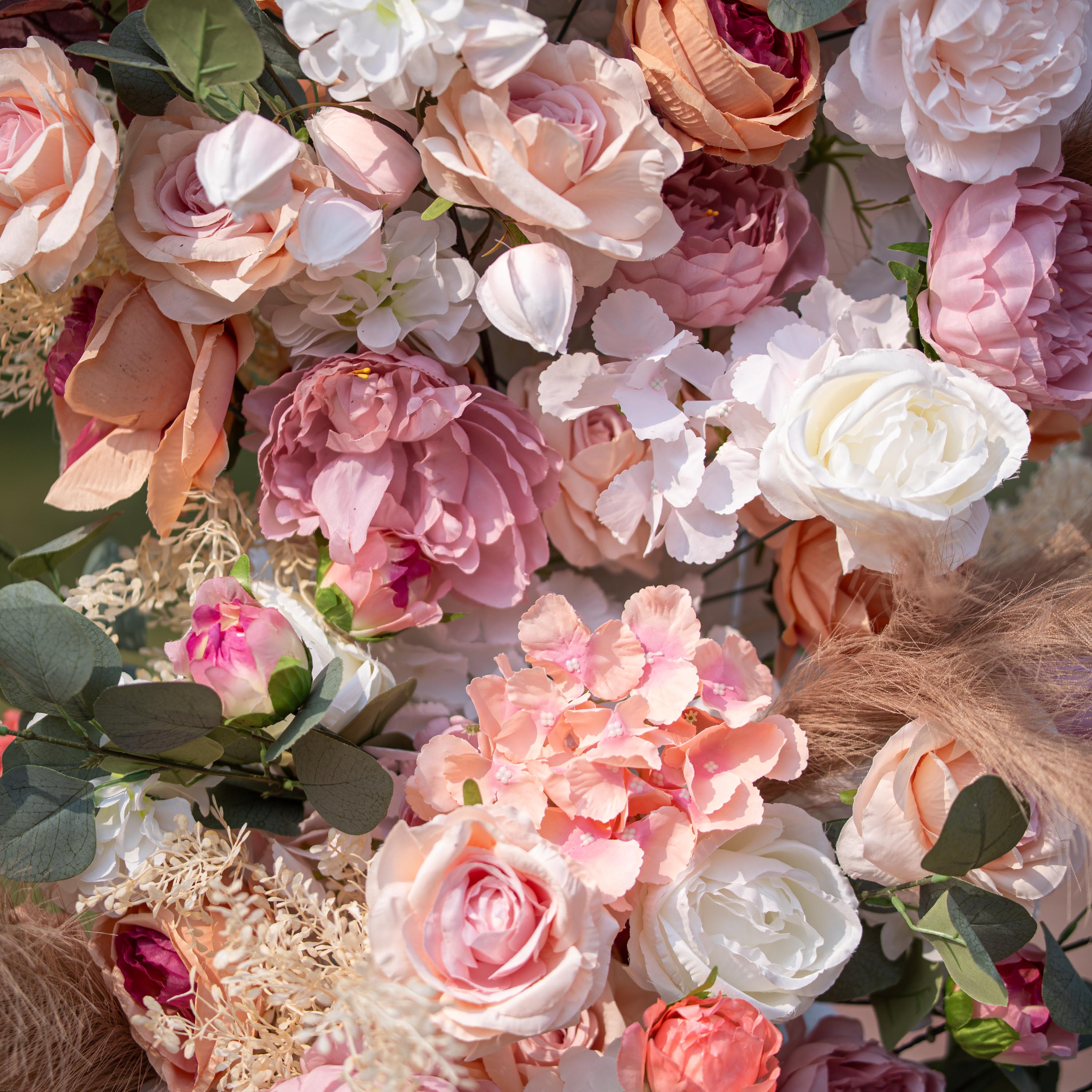 This close - up photo features a rich floral arrangement with roses, peonies, and hydrangeas in soft pink, peach, and white tones. Eucalyptus leaves and pampas grass add texture. With a blurred green backdrop, it exudes a romantic, elegant style, ideal for weddings or upscale garden events.