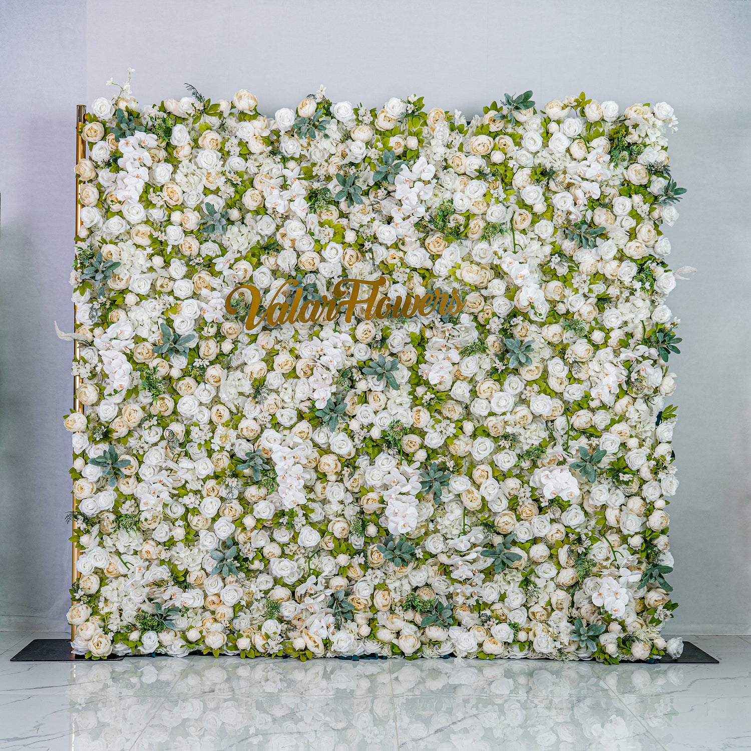 This backdrop is a lush, elegant display of white artificial flowers interspersed with green foliage. Densely packed, it creates a soft, romantic atmosphere. The golden “Valar Flowers” sign adds a touch of sophistication, ideal for weddings or upscale events.