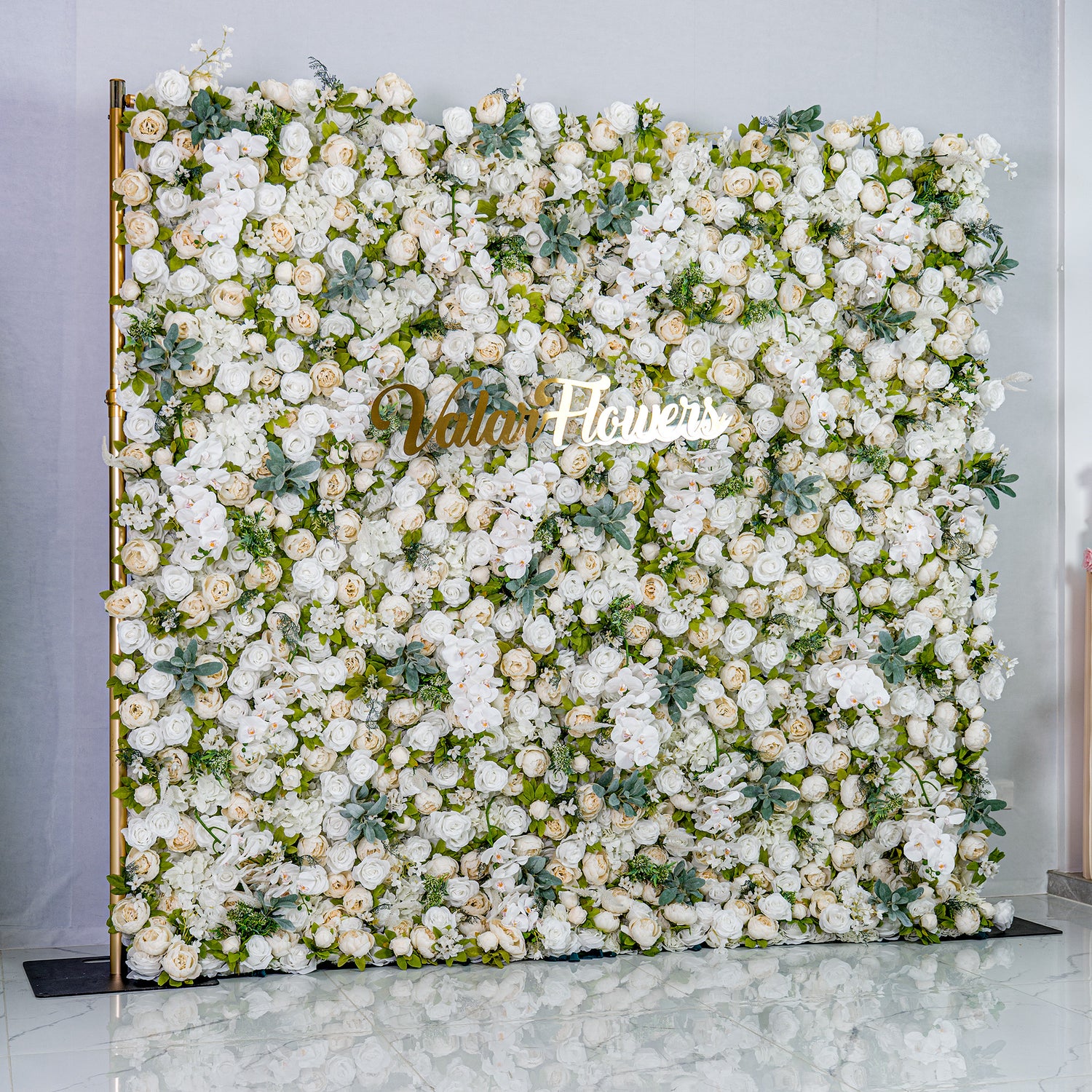 This backdrop is a lush, elegant display of white artificial flowers interspersed with green foliage. Densely packed, it creates a soft, romantic atmosphere. The golden “Valar Flowers” sign adds a touch of sophistication, ideal for weddings or upscale events.