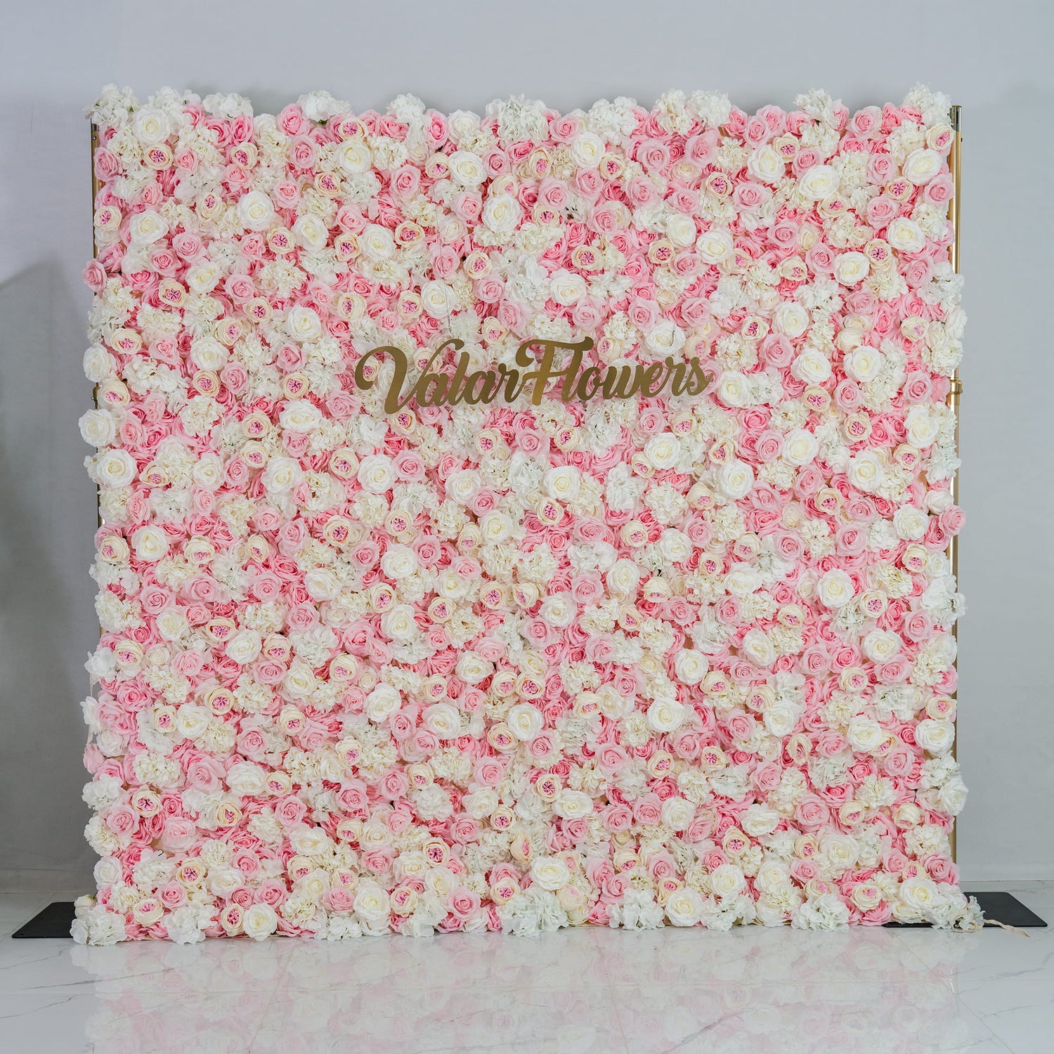 This photo showcases a lush floral backdrop. It is densely covered with a blend of pink and white roses, creating a soft and romantic color scheme. The backdrop also features the text "Valar Flowers" in elegant gold lettering. Ideal for weddings, engagement parties, or bridal showers, it exudes a dreamy and elegant style, perfect for adding a touch of romance to any event.