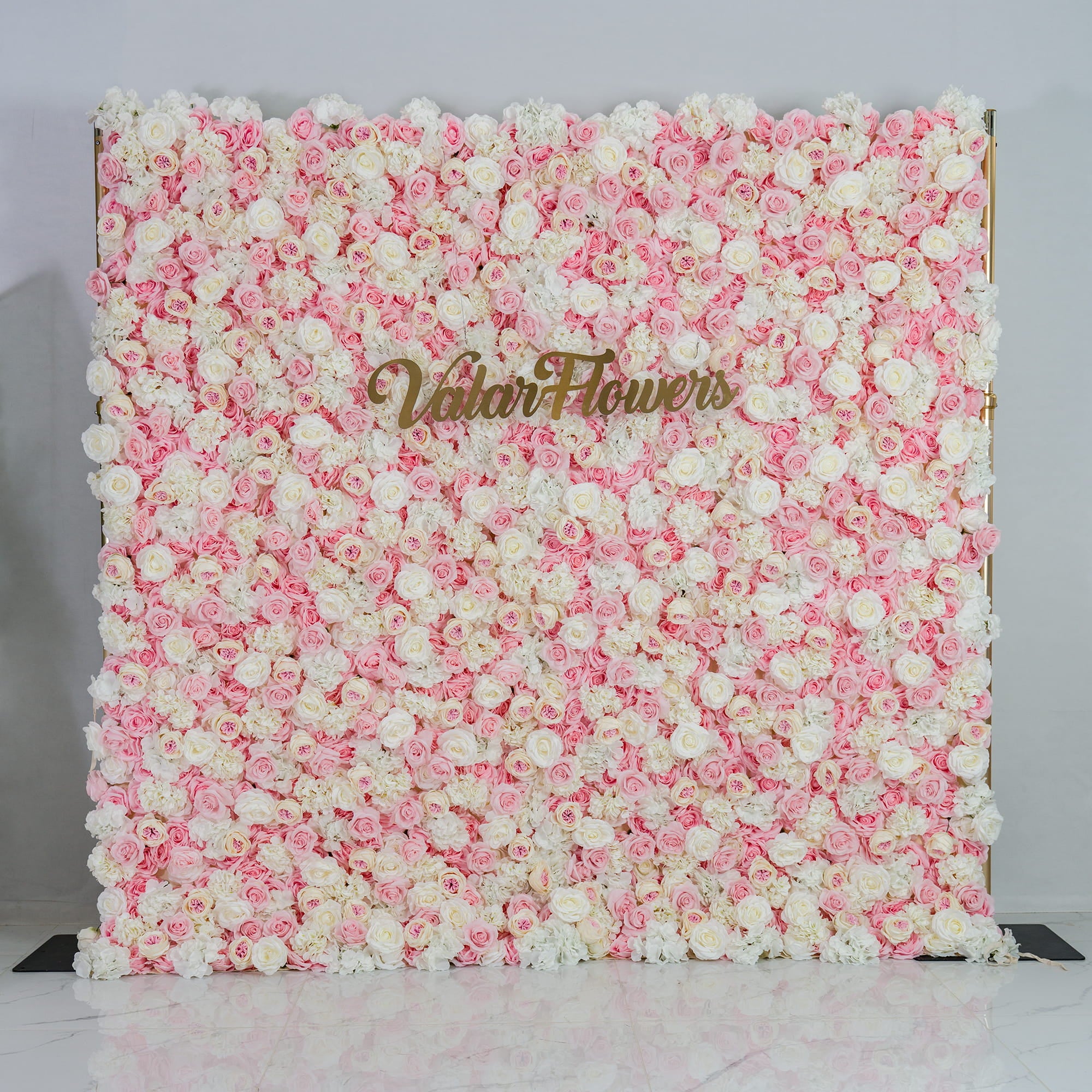 This photo showcases a lush floral backdrop. It is densely covered with a blend of pink and white roses, creating a soft and romantic color scheme. The backdrop also features the text "Valar Flowers" in elegant gold lettering. Ideal for weddings, engagement parties, or bridal showers, it exudes a dreamy and elegant style, perfect for adding a touch of romance to any event.