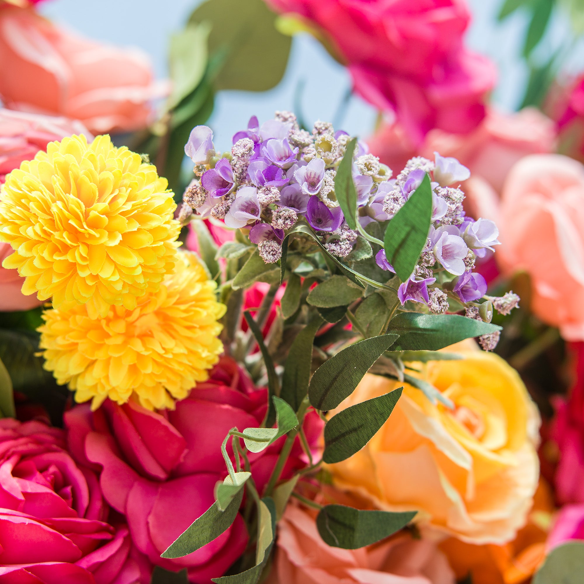 A close - up of a vibrant floral arrangement! Bright yellow pom - pom - like flowers, delicate purple blossoms with tiny white centers, and lush green leaves stand out. Surrounding them are rich pink roses and soft peach - colored blooms. The varied textures and vivid hues create a lively, eye - catching display, perfect for adding a burst of color to any setting.