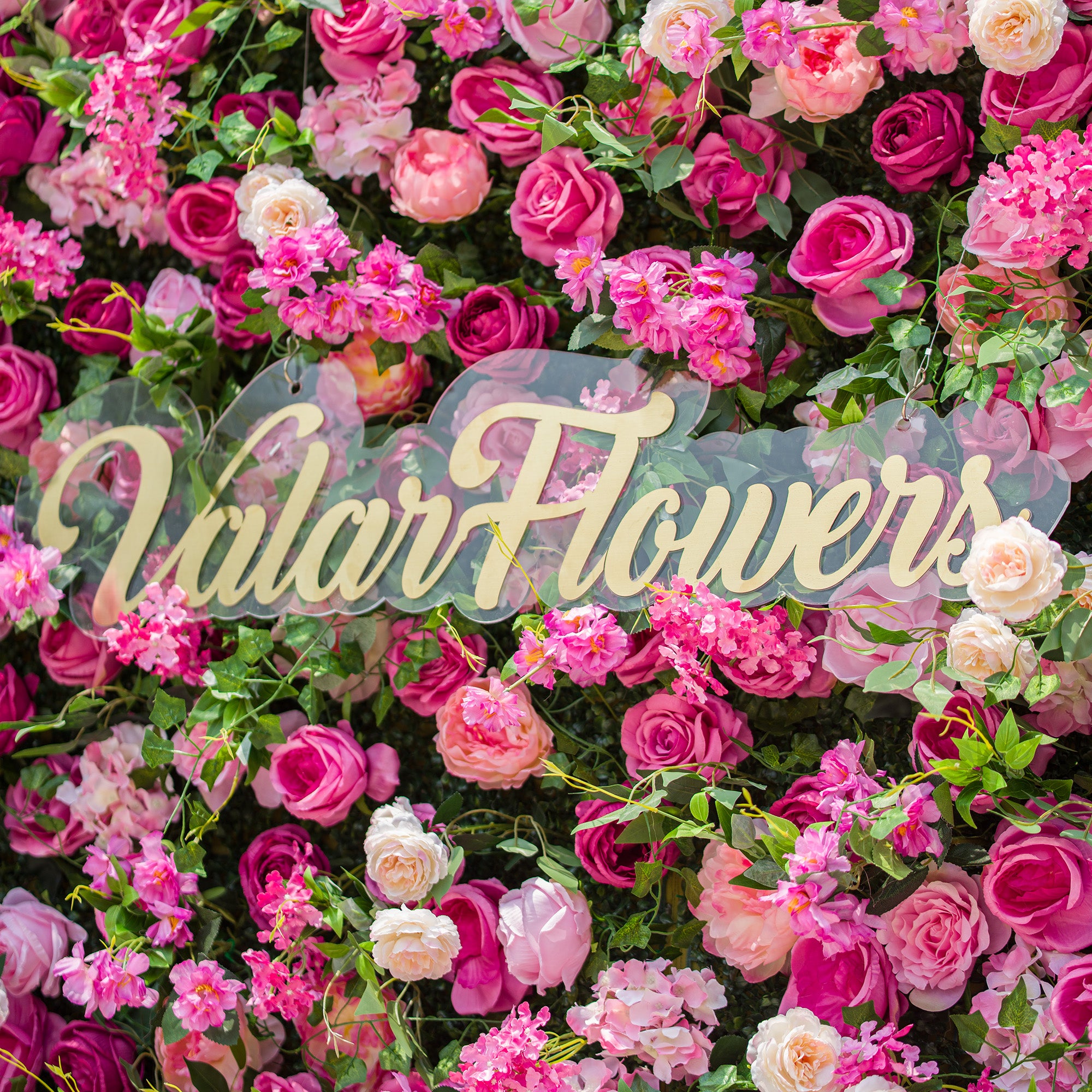 This photo showcases a dense floral backdrop brimming with an array of pink and white roses, along with other assorted pink flowers, all nestled among lush green foliage. The text "ValarFlowers" in elegant golden lettering stands out prominently. The vibrant and abundant blooms create a lively, romantic atmosphere, making it ideal for events like outdoor weddings or spring - themed celebrations.