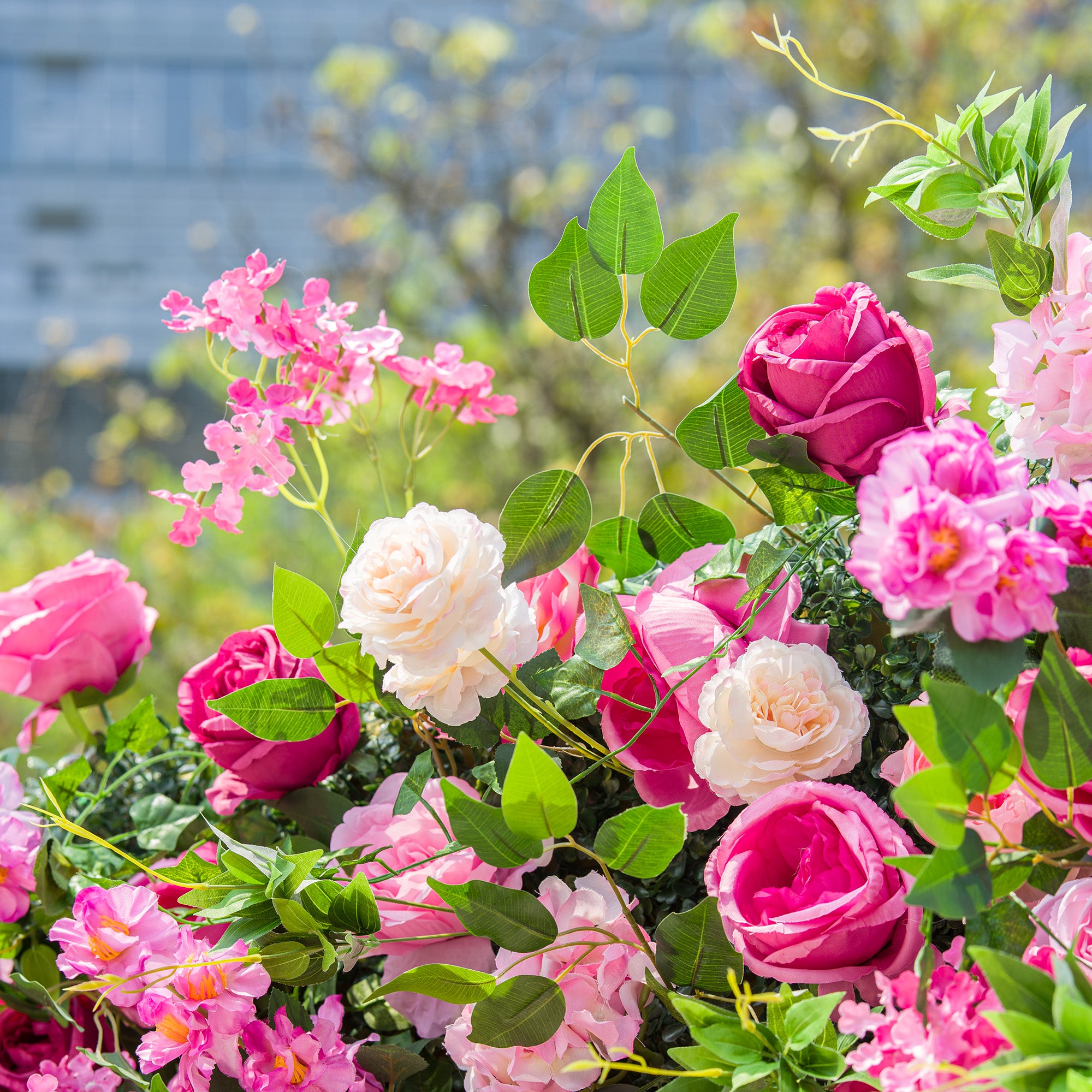 This photo showcases a vibrant floral arrangement with an assortment of pink and white roses, along with other pink flowers, all set against lush green foliage. The bright, colorful blooms create a lively and romantic atmosphere, making it perfect for outdoor events like garden weddings or spring parties.