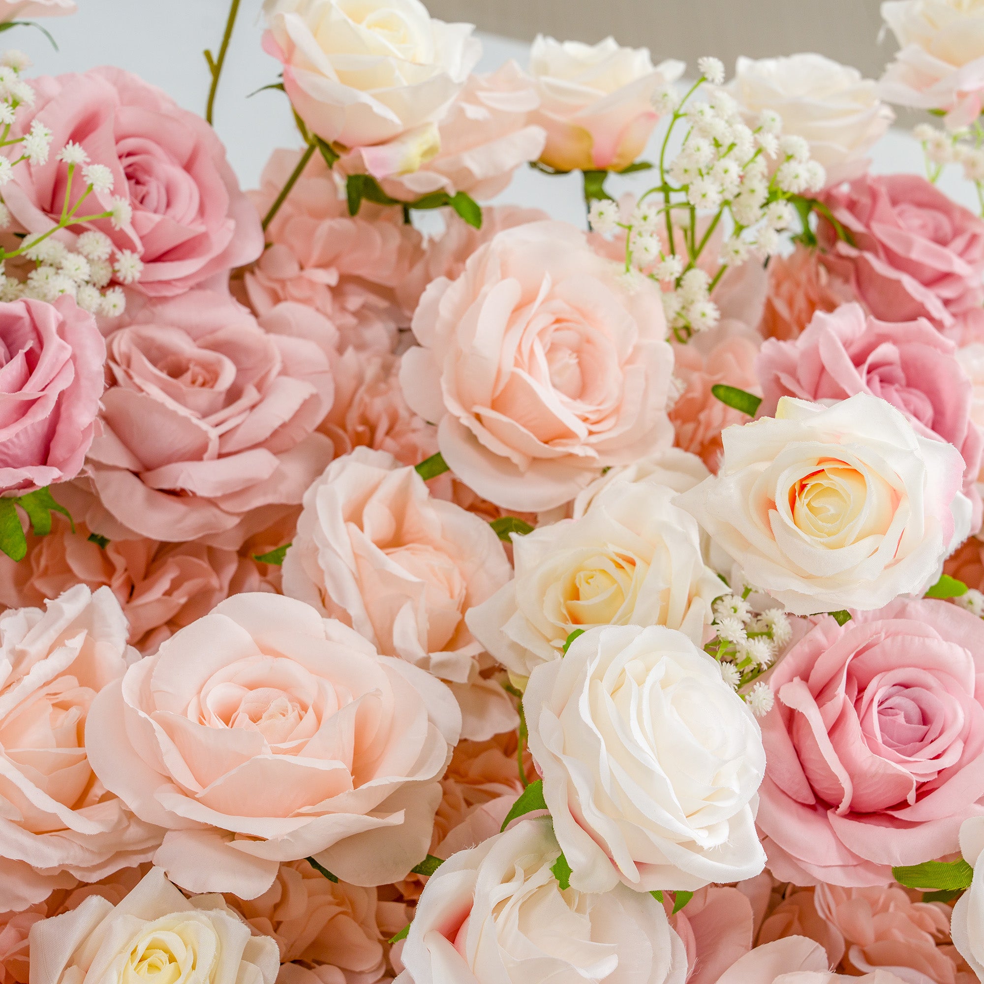 This photo features a lush arrangement of roses in various shades of pink, peach, and white, interspersed with delicate baby&