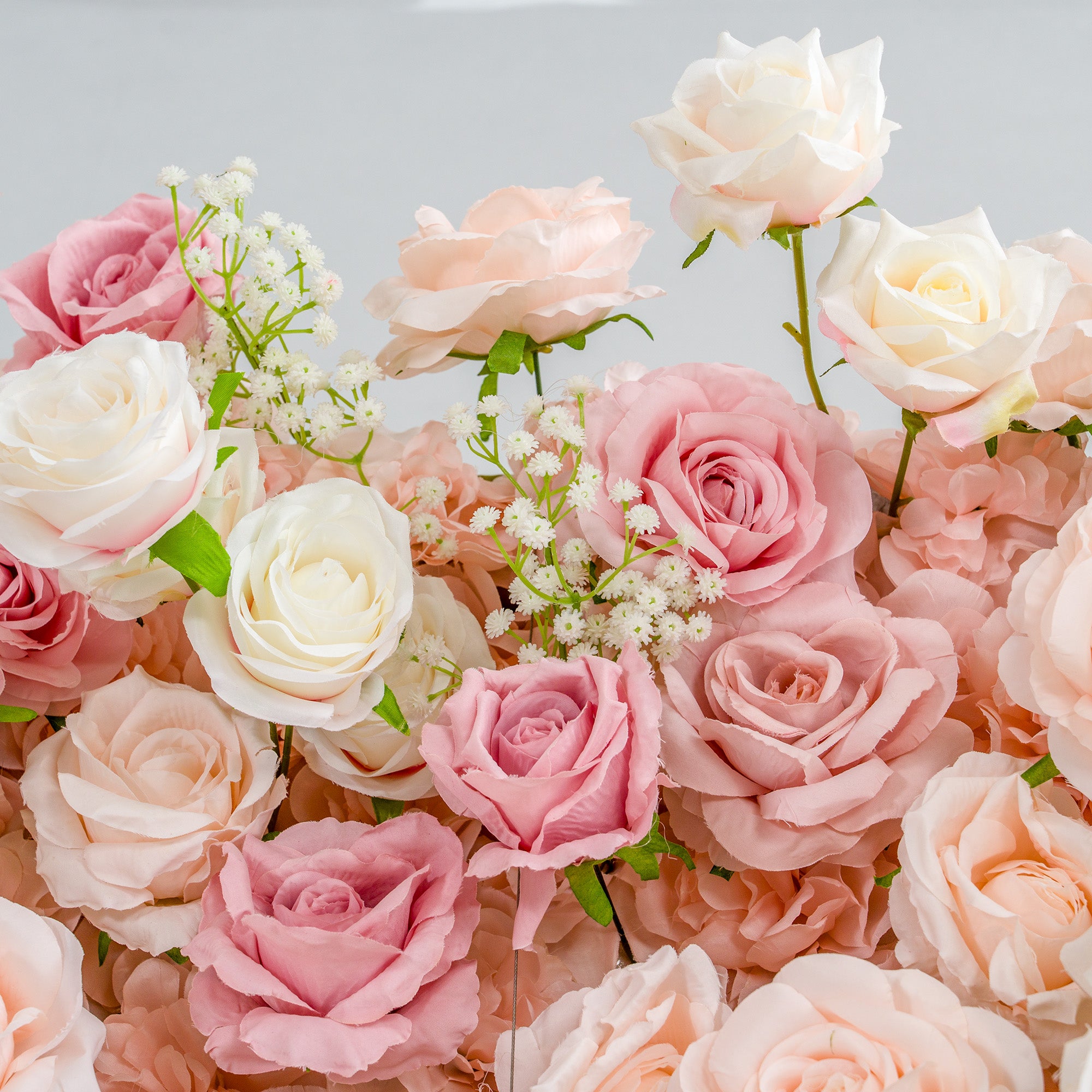 This photo features a lush, vibrant arrangement of roses in soft hues of pink, peach, and white, interspersed with delicate sprigs of baby&
