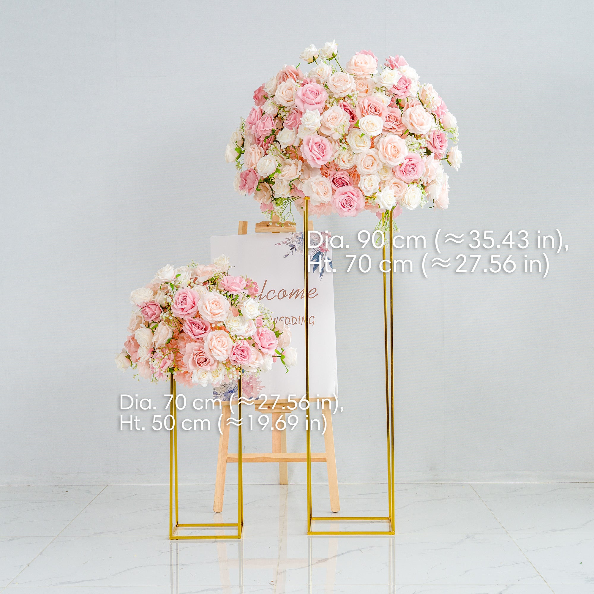 This photo features two elegant floral arrangements on golden stands, composed of pink and white roses with some greenery. The larger arrangement has a diameter of 90 cm (≈35.43 in) and a height of 70 cm (≈27.56 in), while the smaller one has a diameter of 70 cm (≈27.56 in) and a height of 50 cm (≈19.69 in). Behind them is an easel with a "Welcome to our wedding" sign, enhancing the romantic wedding - themed decor.