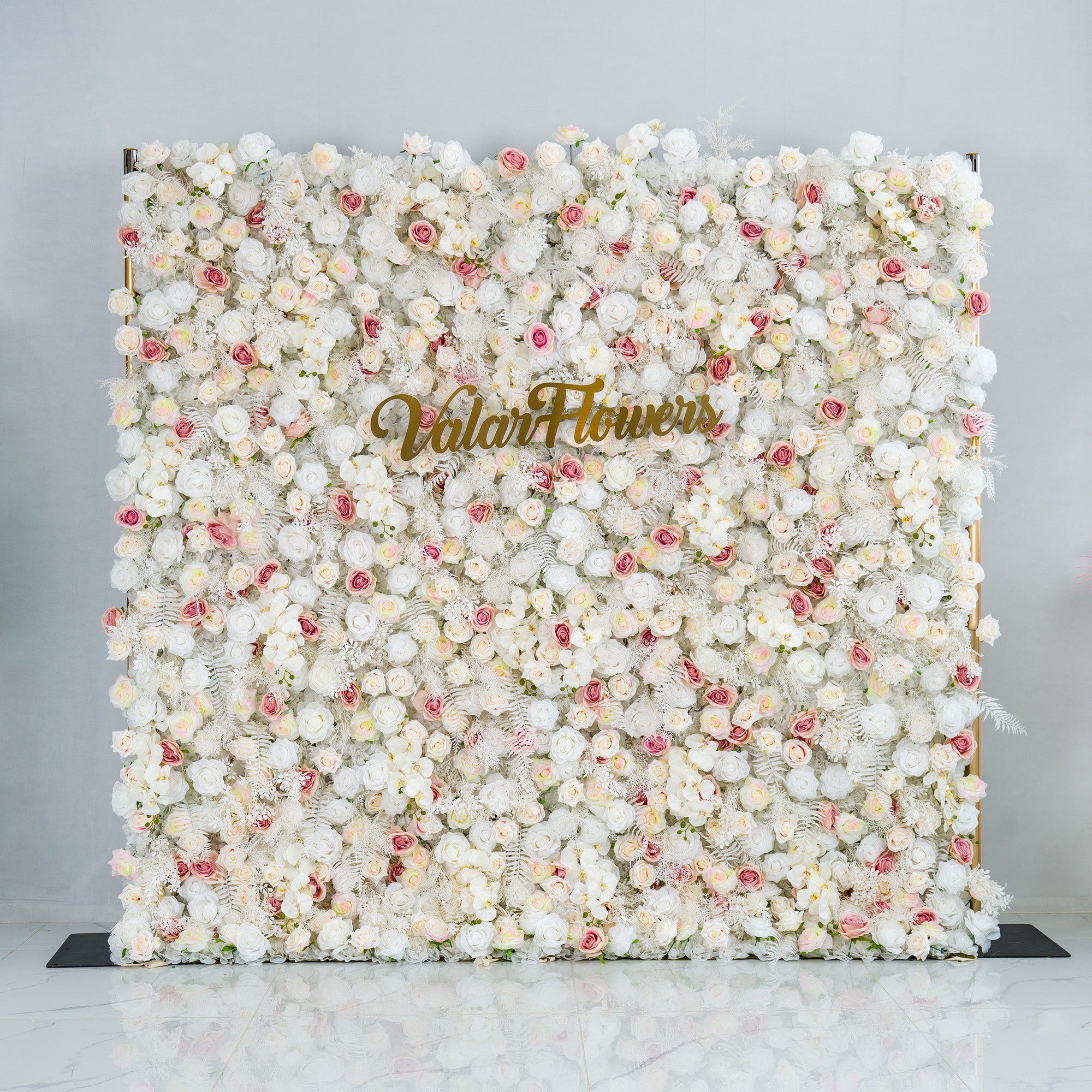 This photo showcases a lush floral backdrop densely covered with white roses and interspersed with delicate pink roses. The soft, neutral color palette creates an elegant and serene atmosphere. The words "Valar Flowers" in elegant gold lettering stand out prominently. Ideal for weddings, upscale galas, or sophisticated events, it exudes a refined and dreamy style.