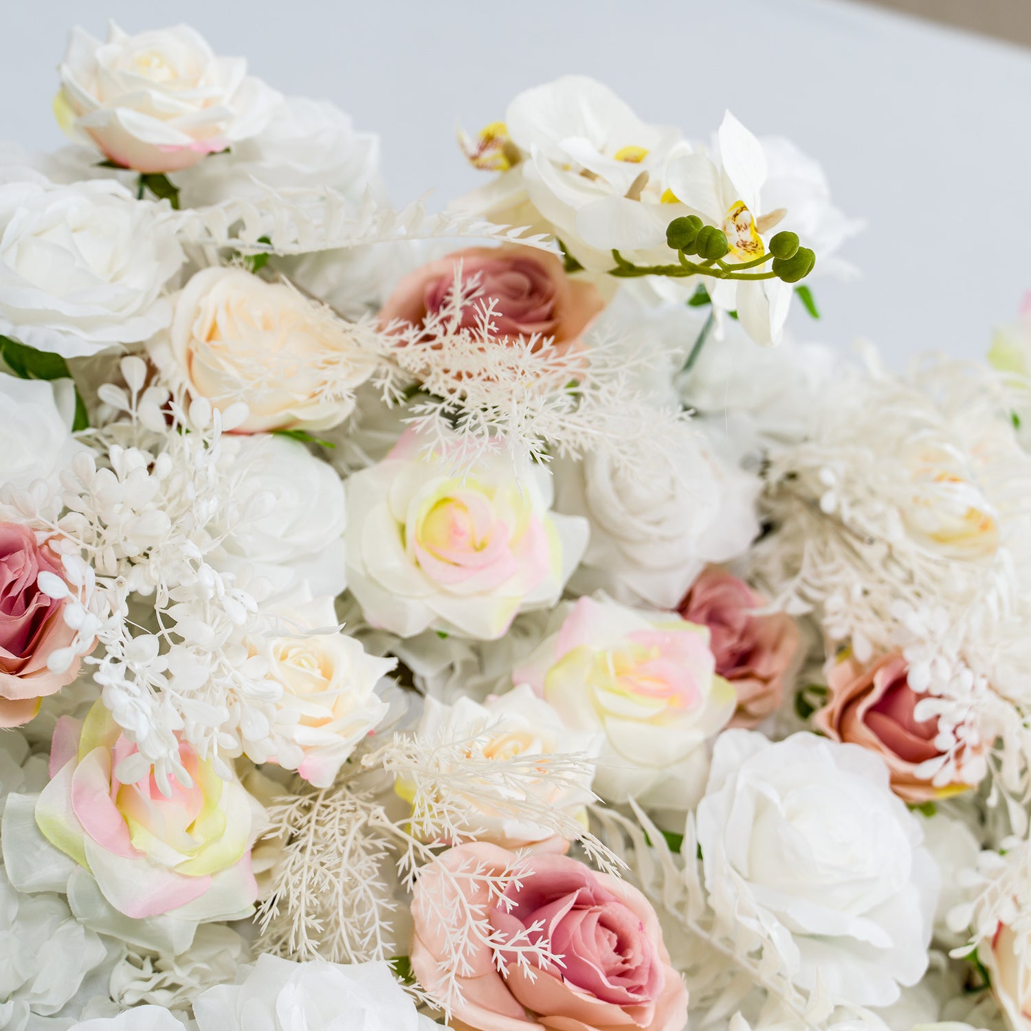 This photo showcases a lush floral arrangement featuring white roses, pink roses with subtle gradients, and white orchids, complemented by delicate white foliage. The soft pastel color palette creates an elegant and serene atmosphere. Ideal for weddings, upscale events, or romantic celebrations, it exudes a refined and dreamy style.