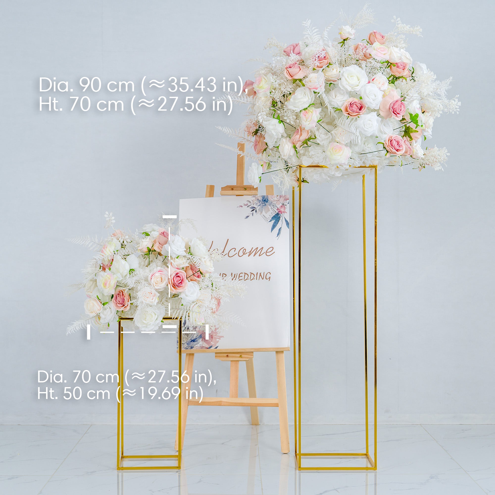 This photo presents a wedding - themed decor setup. Two golden - framed stands hold lush floral arrangements made of white and pink roses, along with white foliage. An easel between them displays a sign that reads "Welcome to our wedding" with floral illustrations. Dimensions of the arrangements are provided, highlighting their elegance and suitability for romantic events.