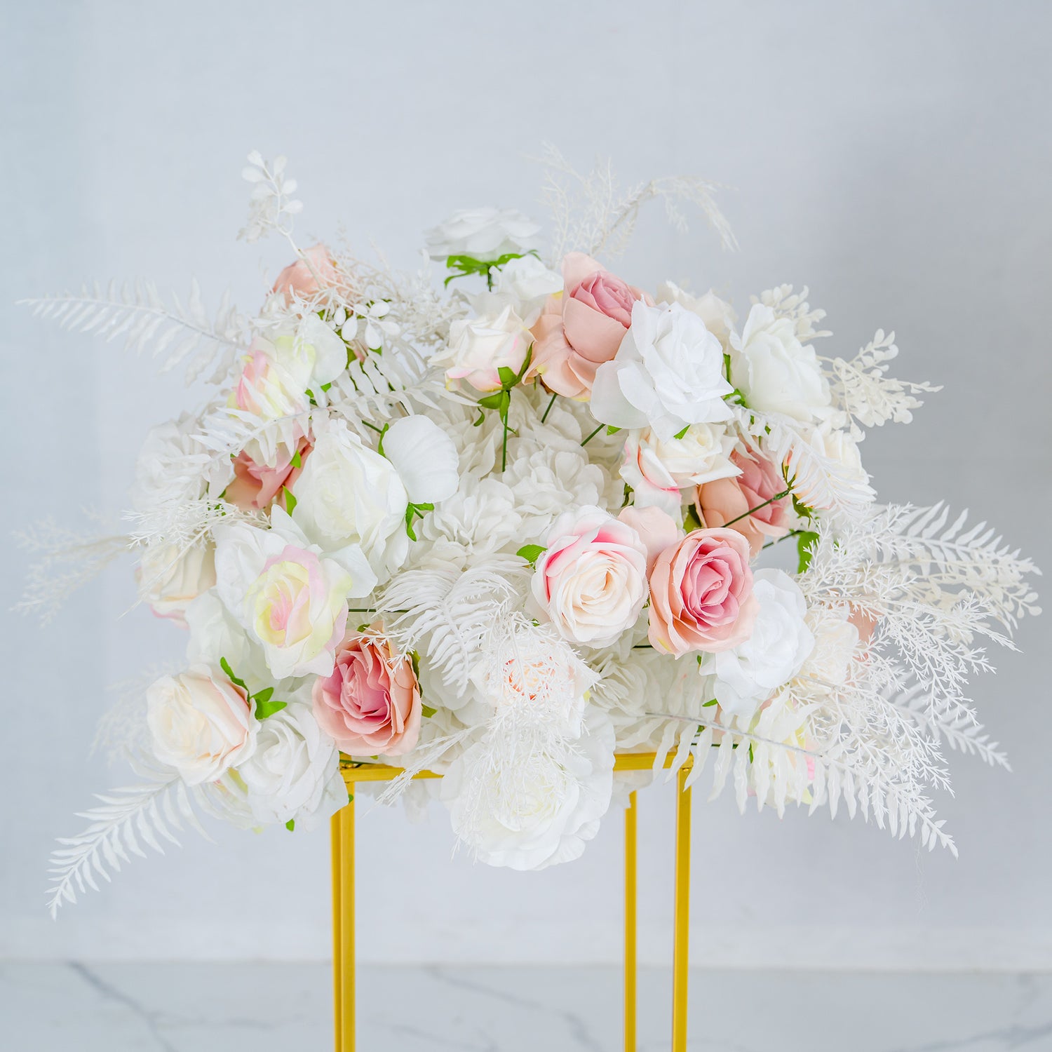 This image showcases a captivating floral arrangement, featuring a harmonious blend of white and pink roses, complemented by delicate white foliage. Arranged in a stylish golden stand, it exudes elegance and charm. Ideal for weddings or upscale events, its soft color palette creates a dreamy ambiance. Perfect for enhancing event decor.