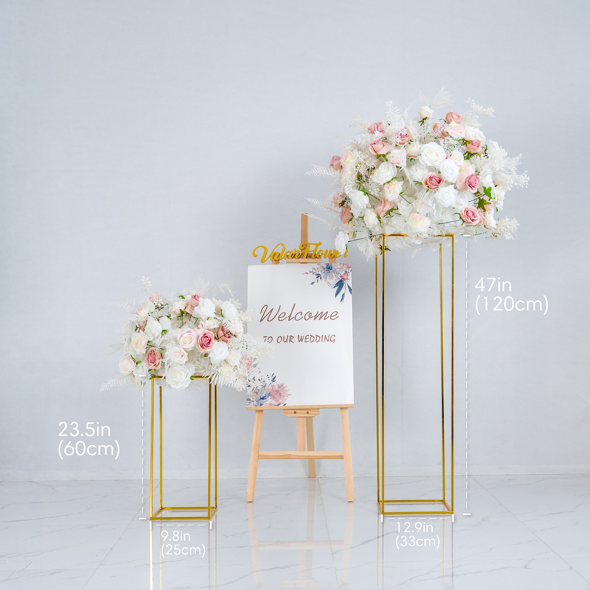 This photo shows a wedding - themed decor setup. Two golden - framed floral arrangements, filled with white and pink roses and white foliage, stand on either side of an easel. The easel holds a sign that reads "Welcome to our wedding" with floral illustrations. The smaller arrangement is 23.5 inches (60cm) tall, the larger one is 47 inches (120cm), with base dimensions provided. It exudes an elegant and romantic style.