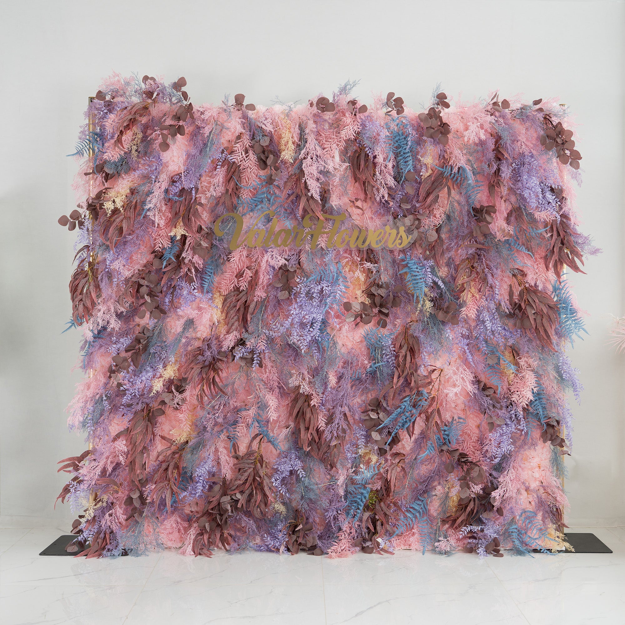 This backdrop is a lush, colorful foliage arrangement. It features a blend of pink, purple, and brown leaves, with some blue fern - like fronds adding contrast. The elegant "Valar Flowers" sign in gold lettering stands out amidst the greenery. Ideal for weddings, parties, or upscale events, it exudes a romantic and sophisticated style.