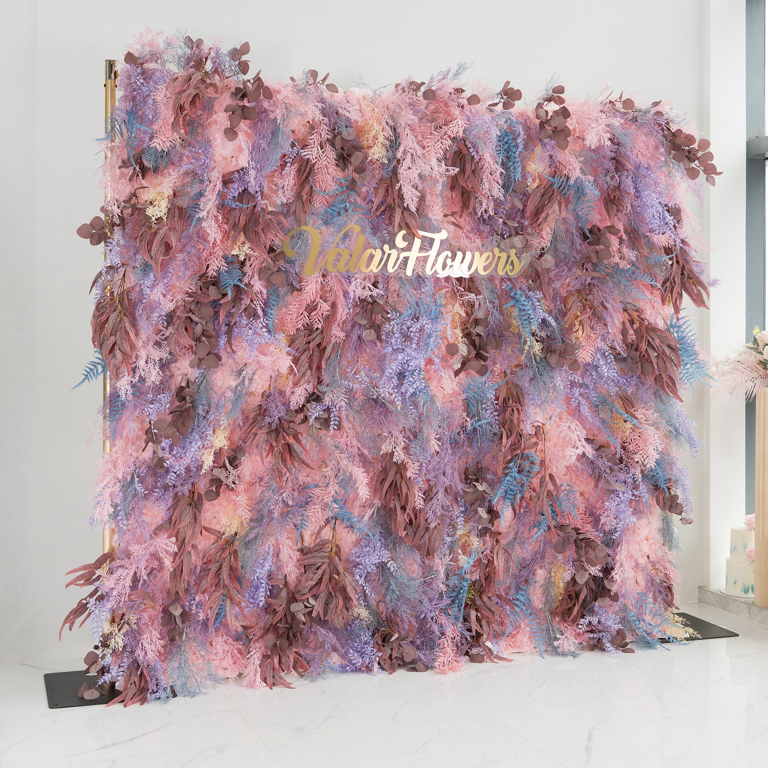 This backdrop is a vibrant and lush foliage display. It combines a dreamy palette of pinks, purples, and blues, interspersed with earthy brown leaves. The elegant gold text "Valar Flowers" is prominently featured. Ideal for weddings, galas, or upscale parties, it exudes a romantic and whimsical style, creating a visually captivating scene.