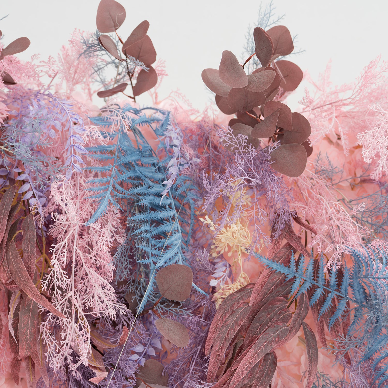 This photo showcases a lush foliage arrangement with a dreamy color palette. It features fern - like fronds in blue and purple, alongside eucalyptus leaves in earthy brown tones, all mixed with soft pink foliage. Ideal for events like weddings, bridal showers, or upscale parties, it exudes a romantic and whimsical style, creating a visually captivating backdrop.