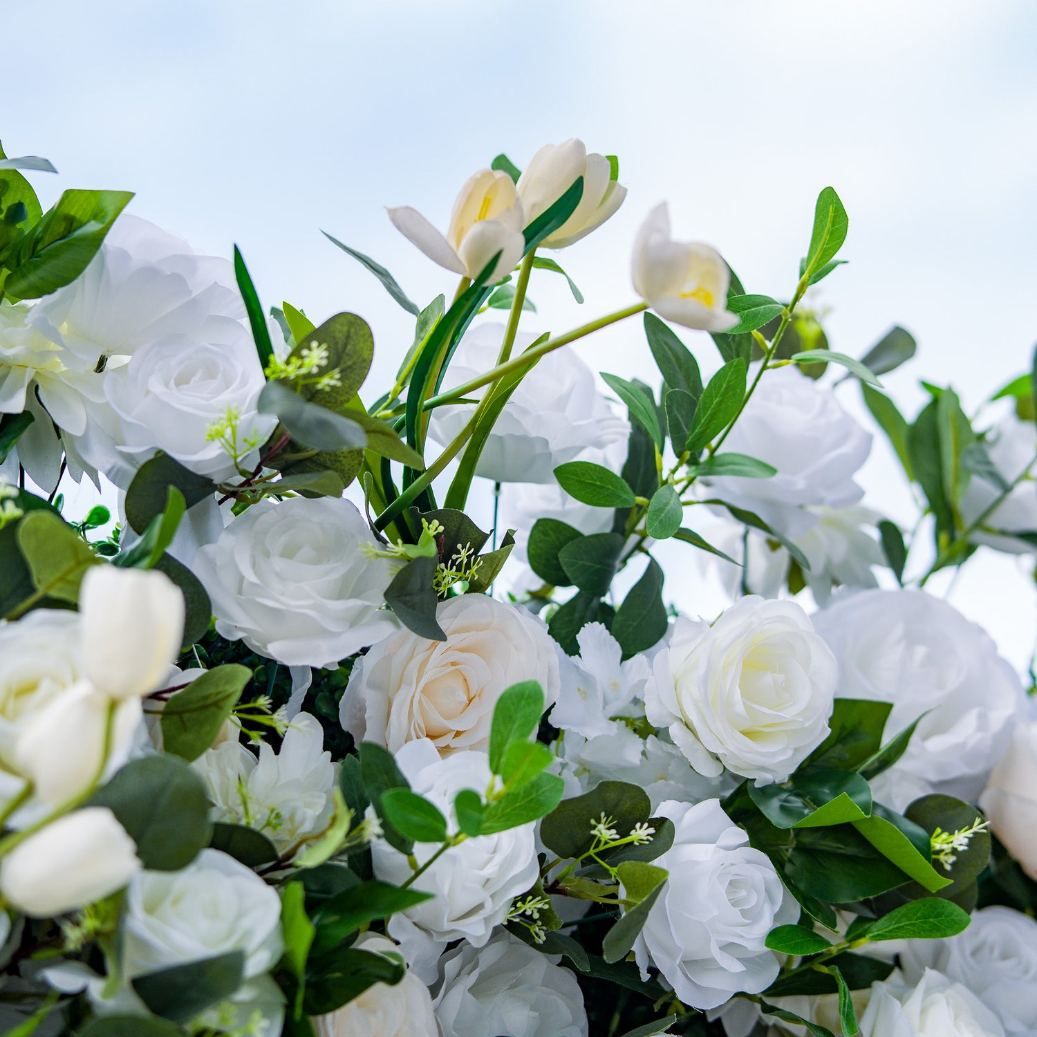 This photo features a lush arrangement of white roses and tulips, interspersed with green foliage. The delicate white blooms create an elegant and serene display. Ideal for events like a “White - Tie Garden Gala” or a refined wedding, it exudes a sense of sophistication and purity, perfect for upscale and graceful celebrations.