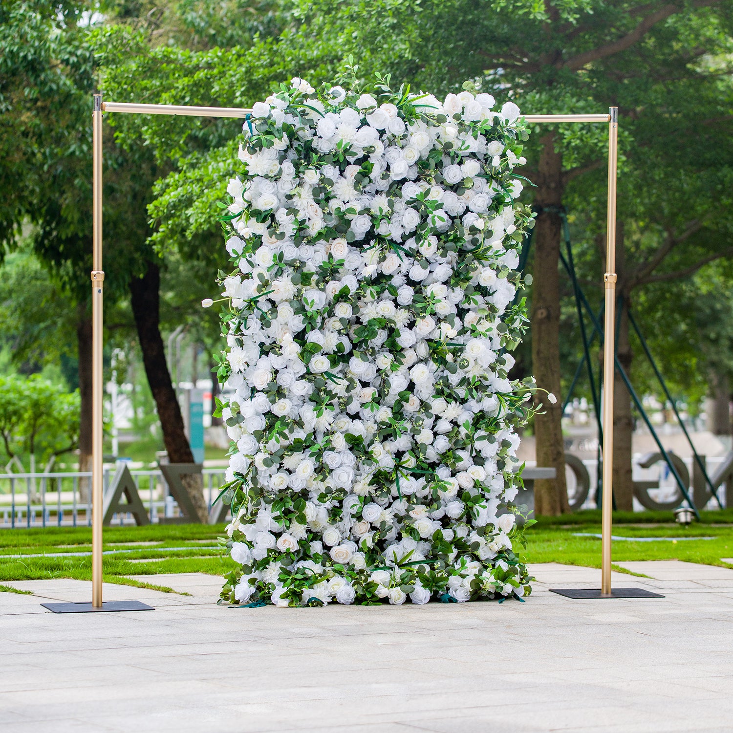 This photo showcases a 4*8ft floral backdrop densely covered with white roses and tulips, interspersed with lush green foliage. Set against a park - like background, it exudes elegance. Ideal for events like a “White Grace” wedding or a sophisticated garden reception, it creates a refined and serene atmosphere for upscale outdoor celebrations.